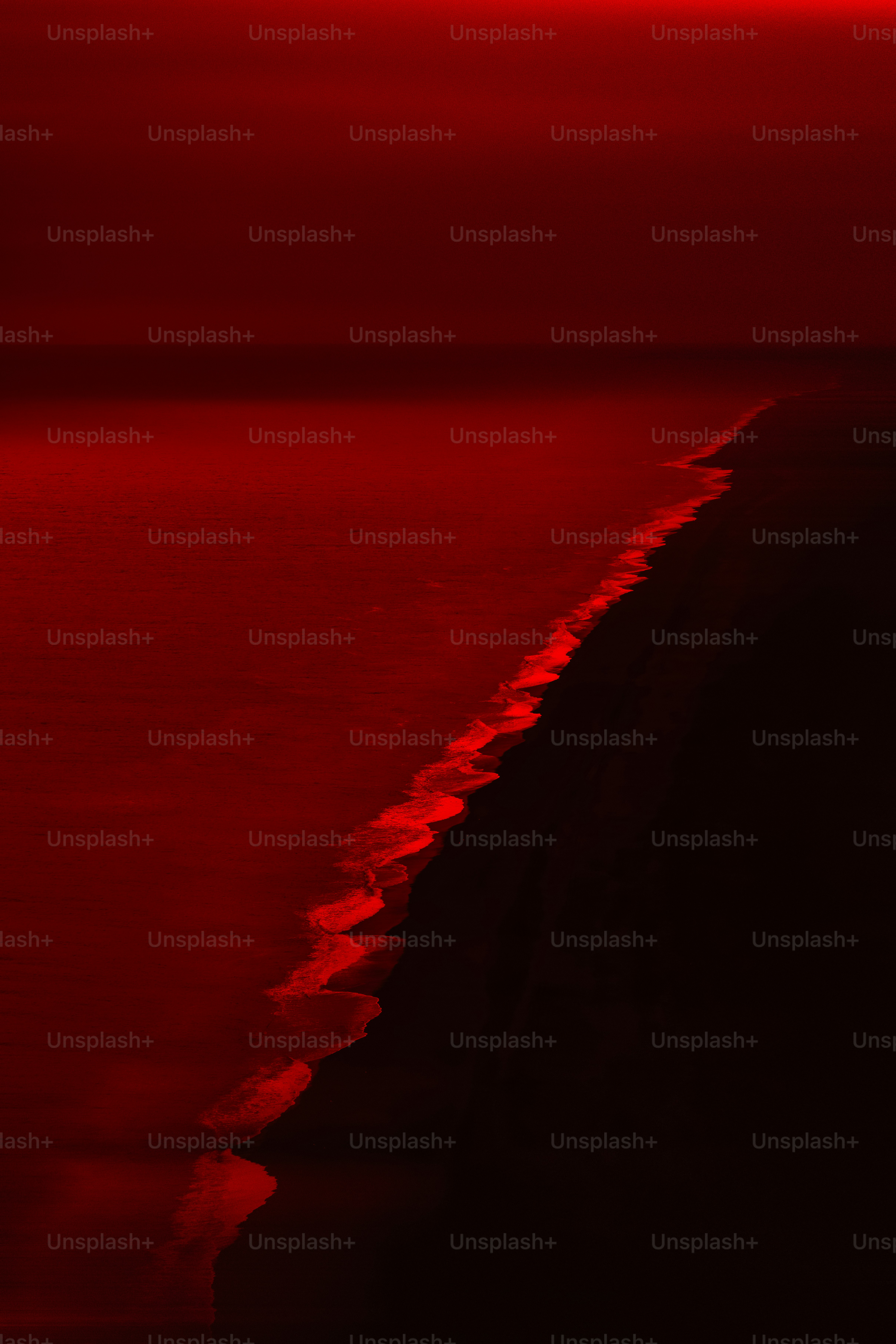 Una costa scura con onde rosse brillanti che si infrangono contro una spiaggia nera di sabbia