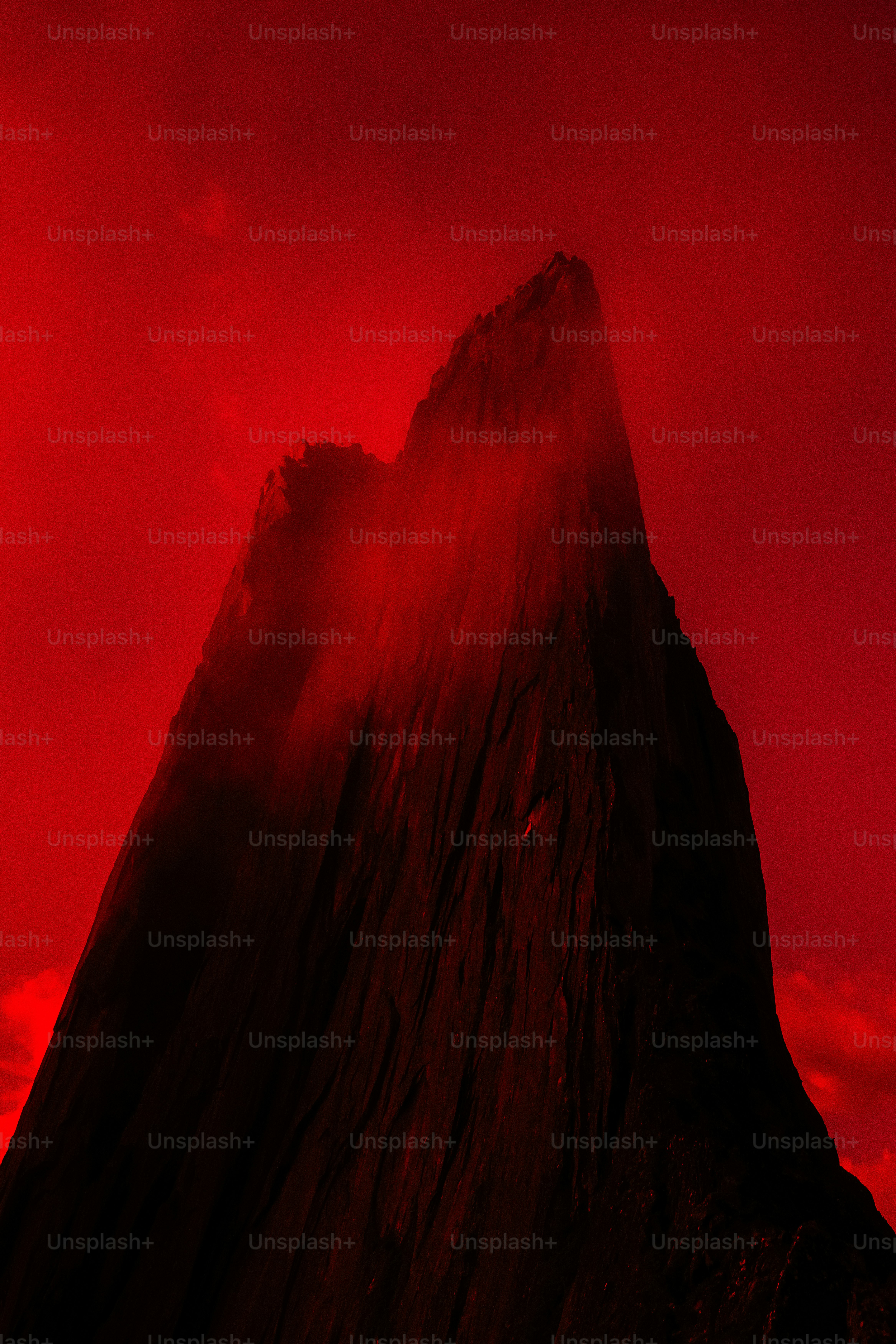 Una vetta di montagna frastagliata controluce contro un cielo rosso vibrante con filamenti di nuvole