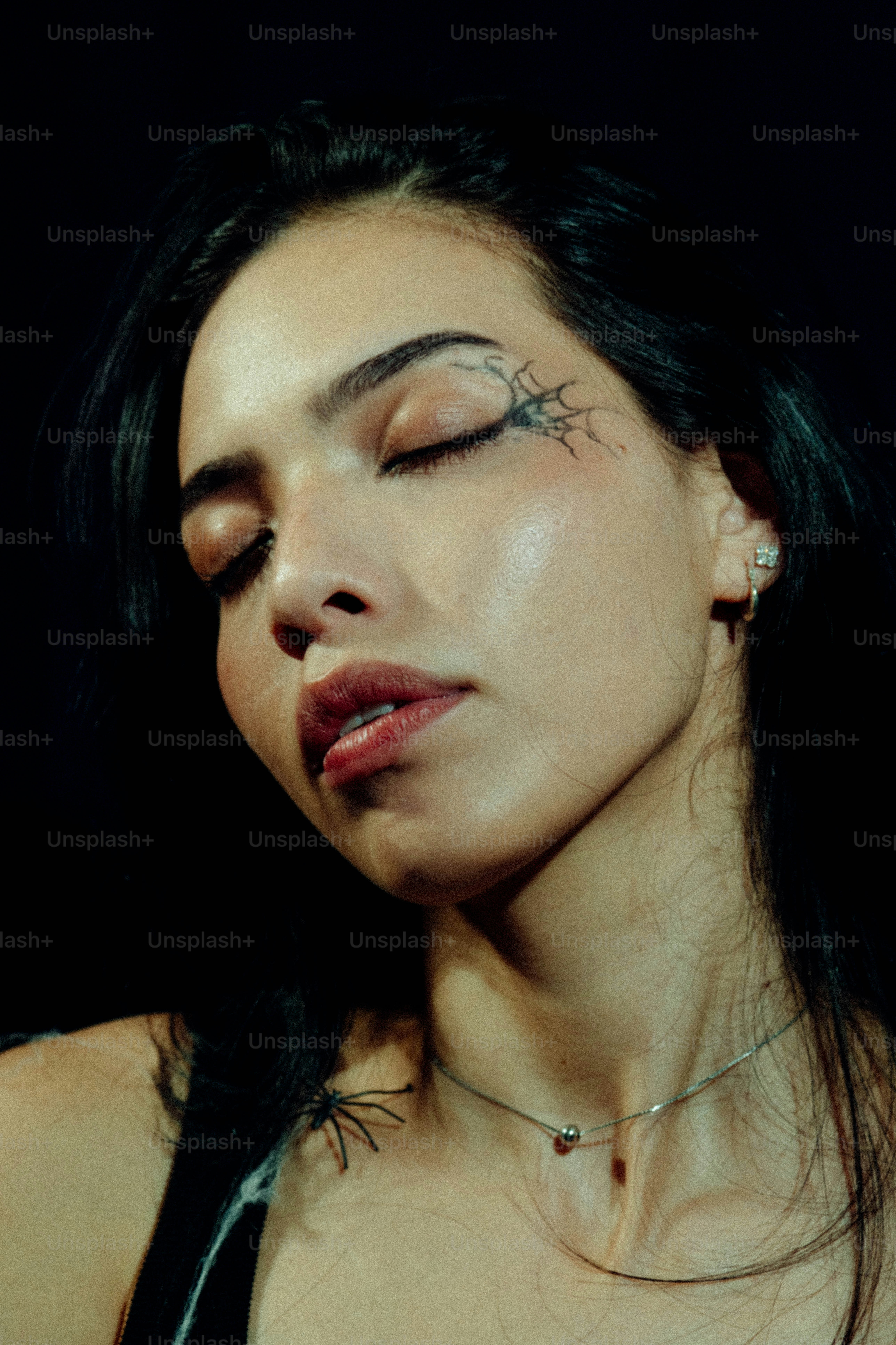 Uma mulher de olhos fechados e uma tatuagem em forma de teia de aranha perto do olho