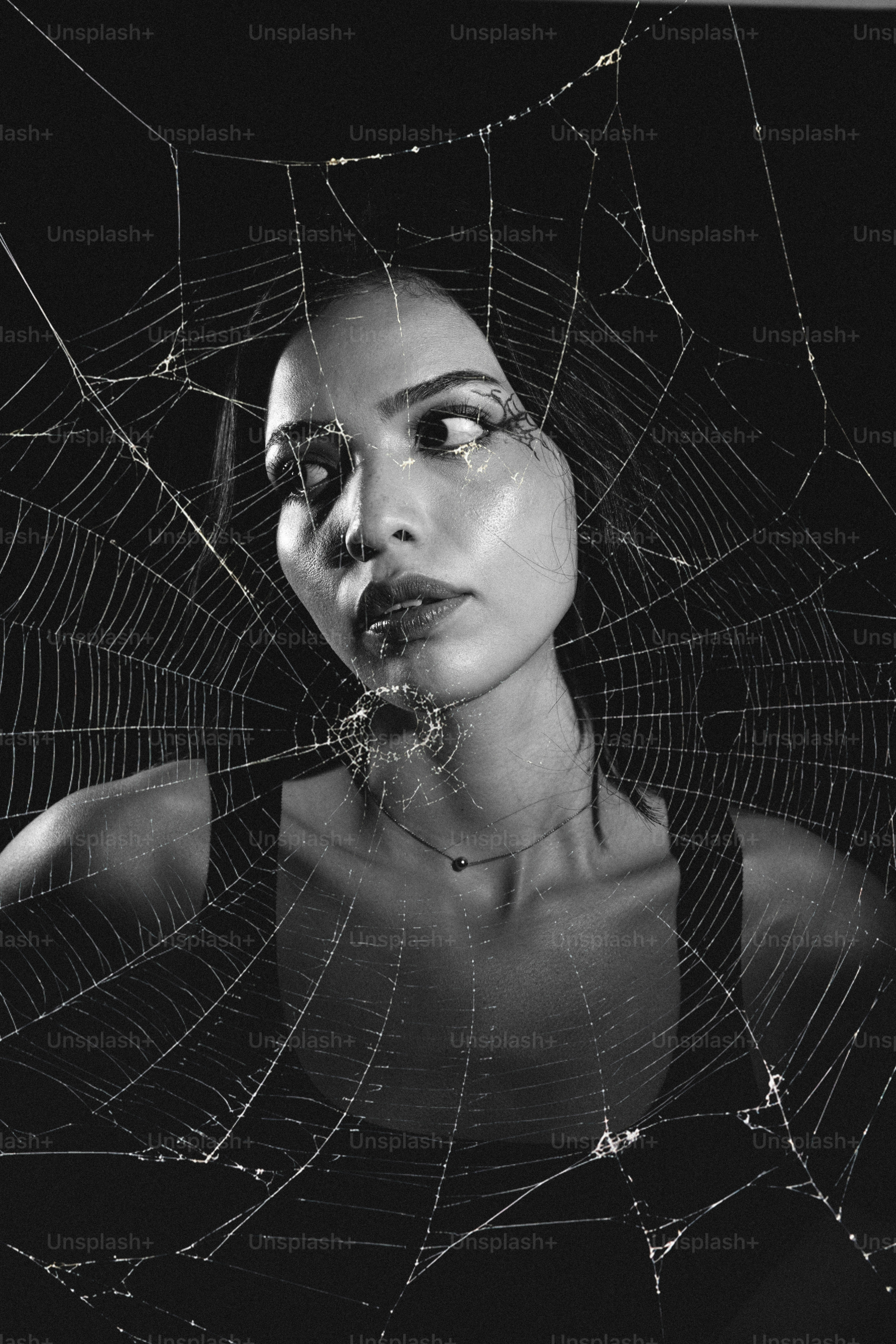 Uma mulher olhando através de uma teia de aranha contra um fundo escuro