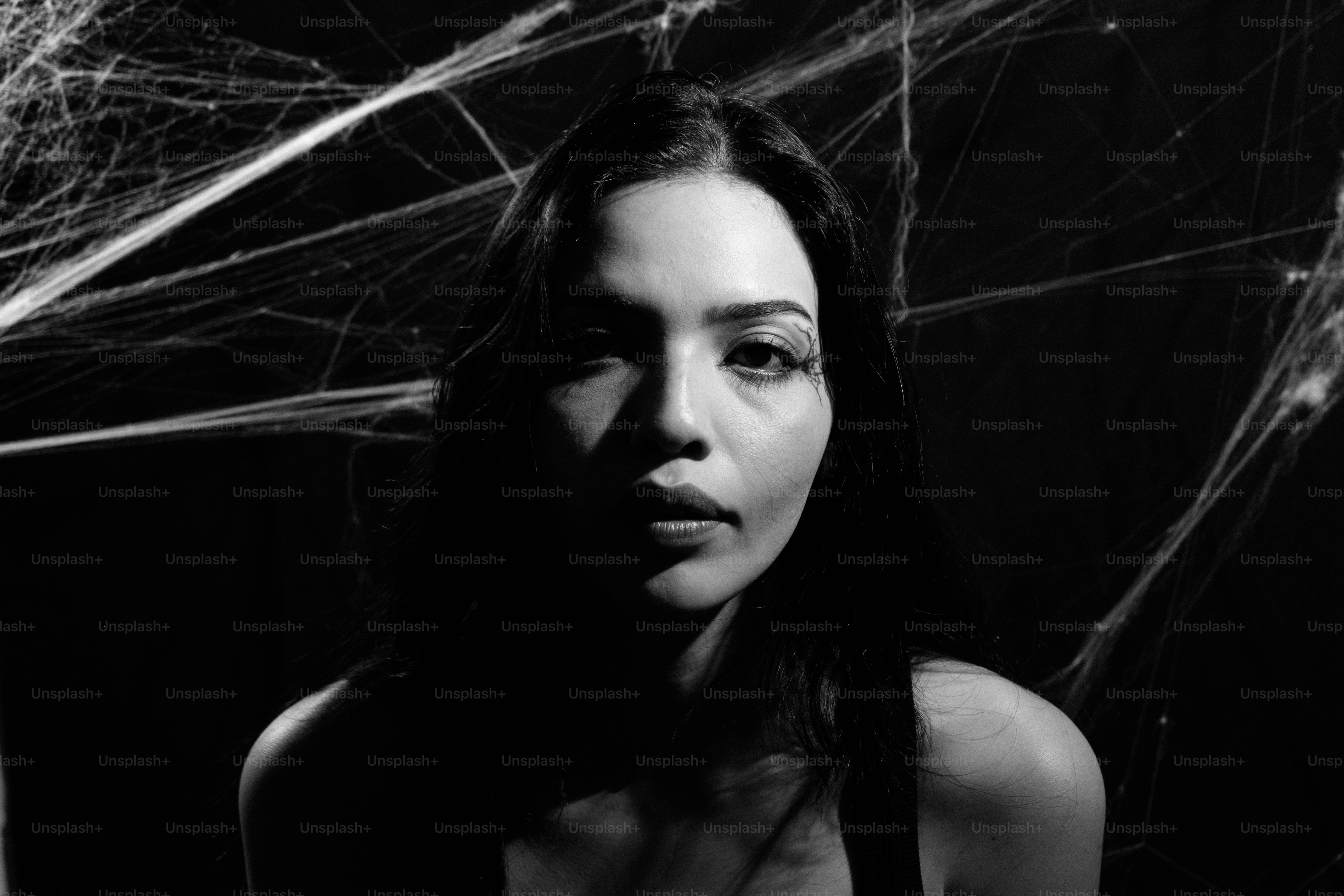 Uma mulher de cabelo escuro contra um fundo preto com teias de aranha brancas