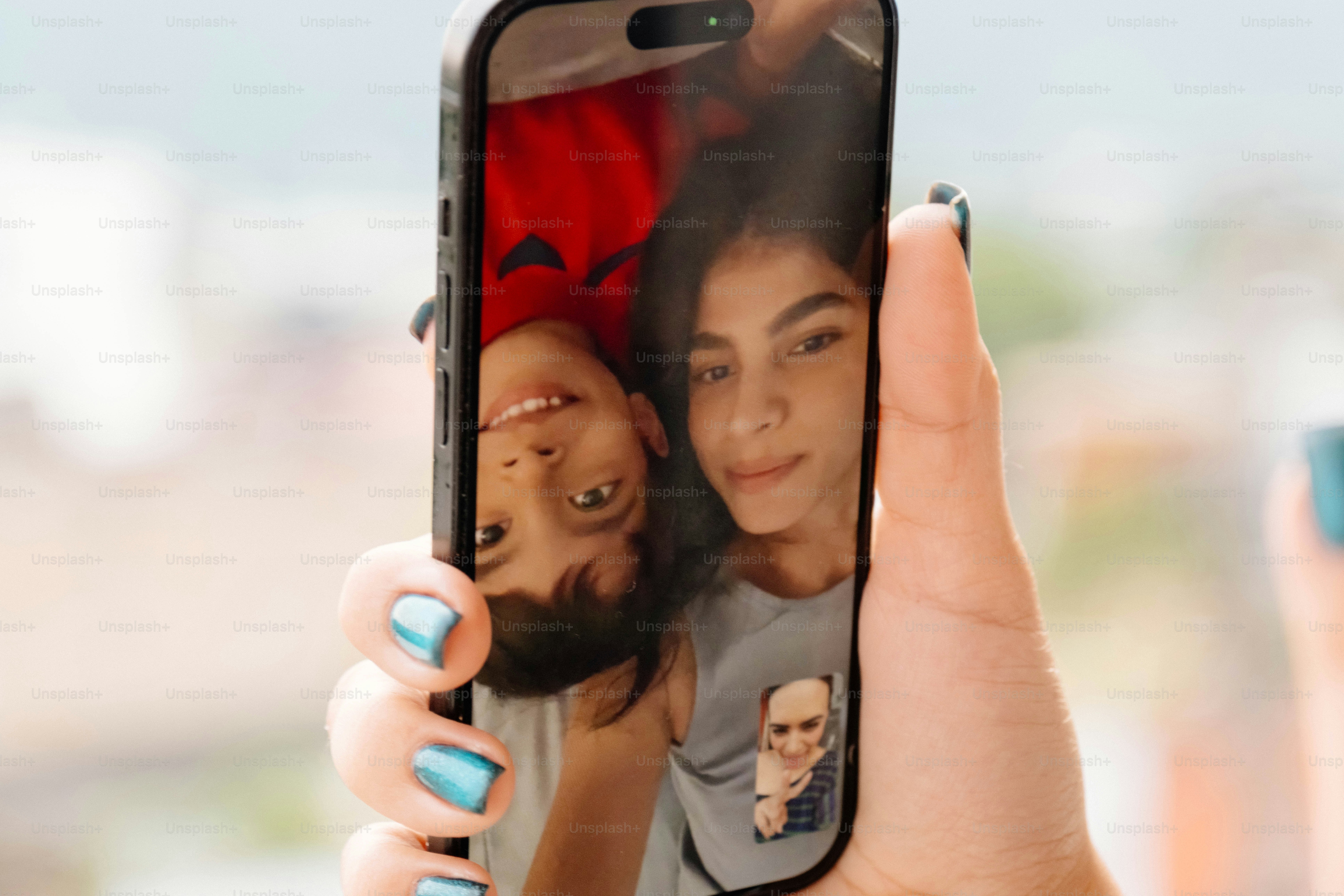 Uma mão segurando um smartphone exibindo uma videochamada com uma mulher e uma criança