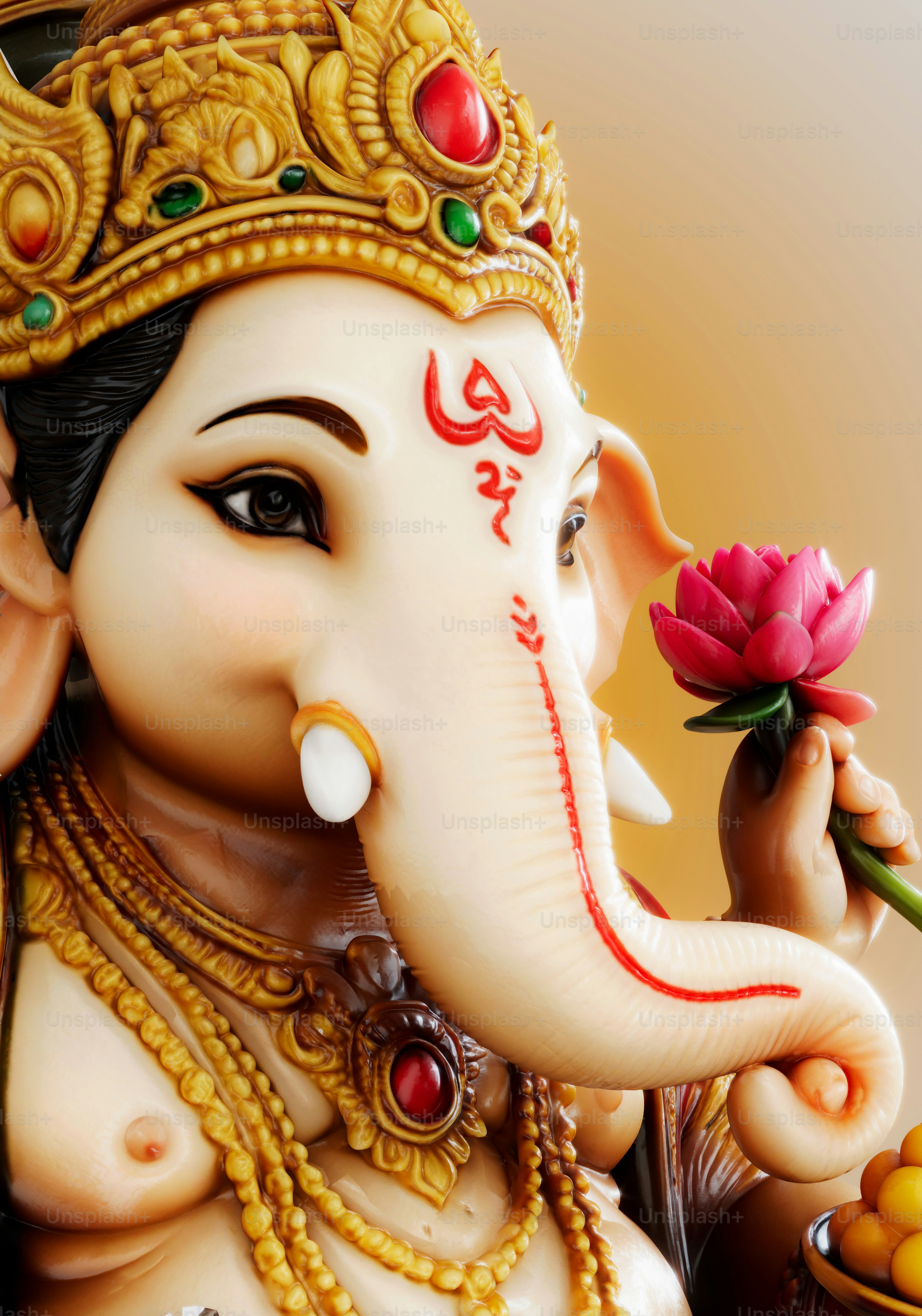 Una estatua de Ganesha con una corona dorada y sosteniendo una flor de loto rosa
