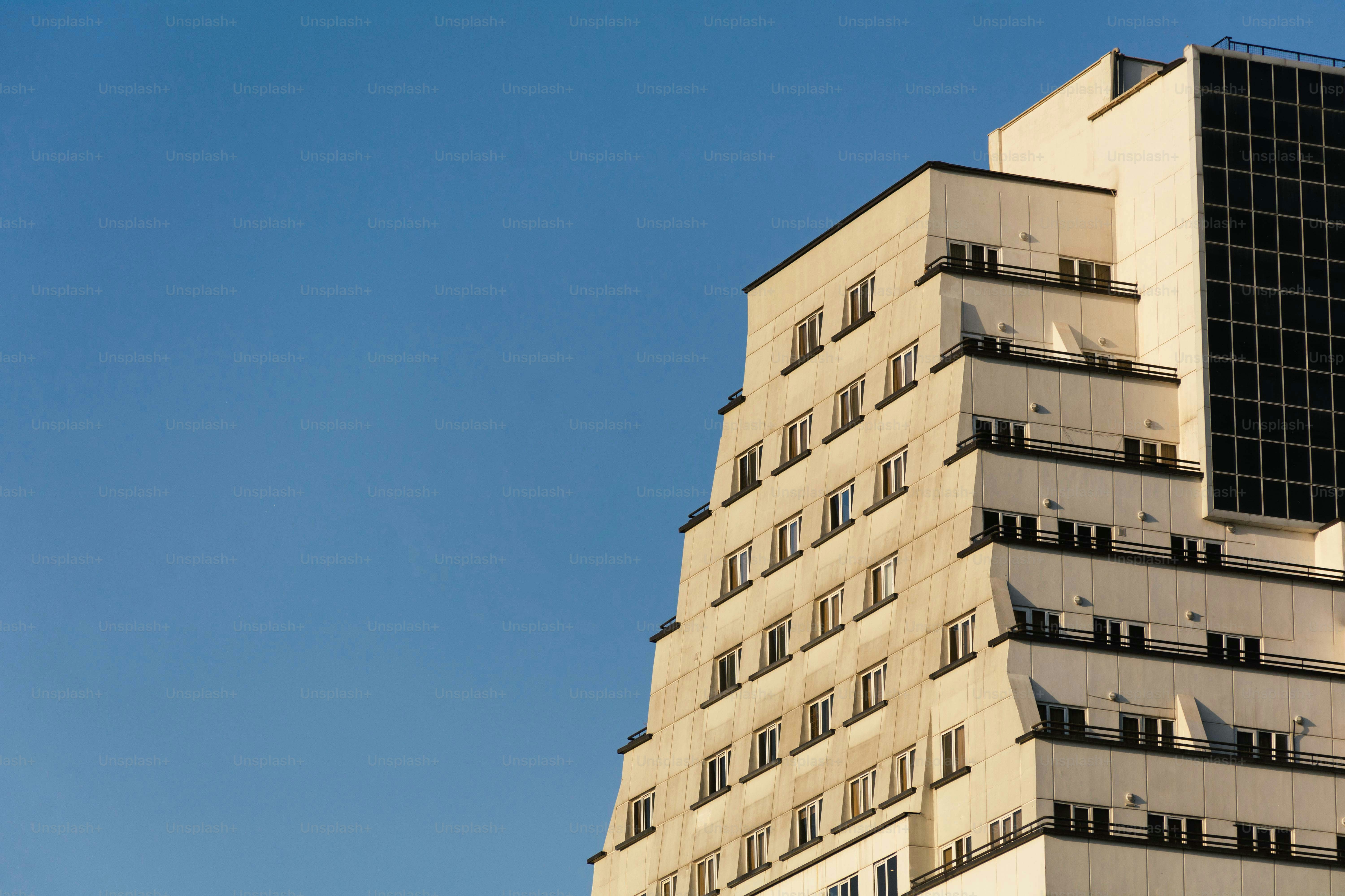 Ein stufiges weißes Wohnhaus mit Balkonen vor klarem blauen Himmel