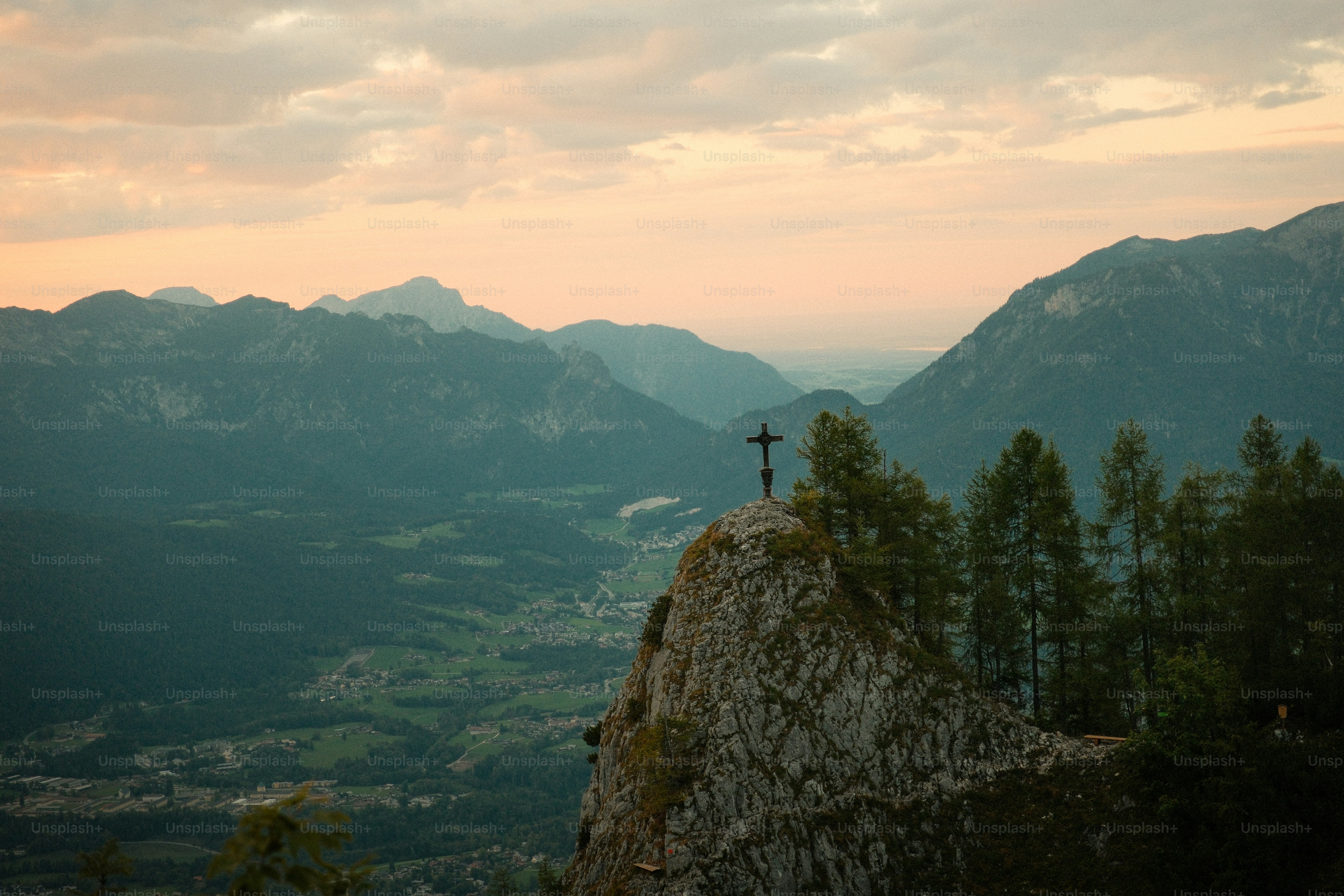 A metal cross on a rocky mountain peak overlooking a valley at golden hour