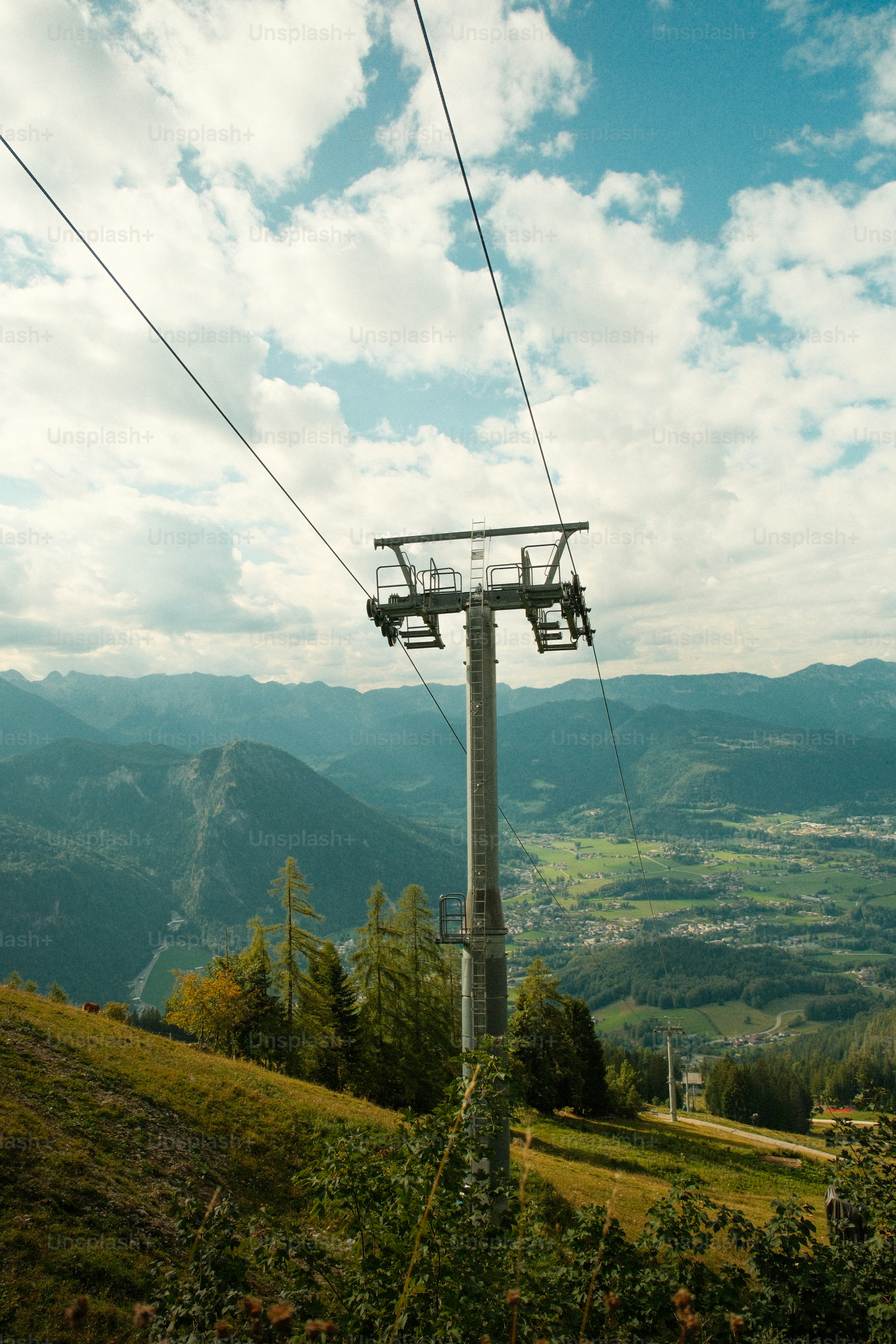 A ski lift tower on a grassy mountain slope overlooking a green valley