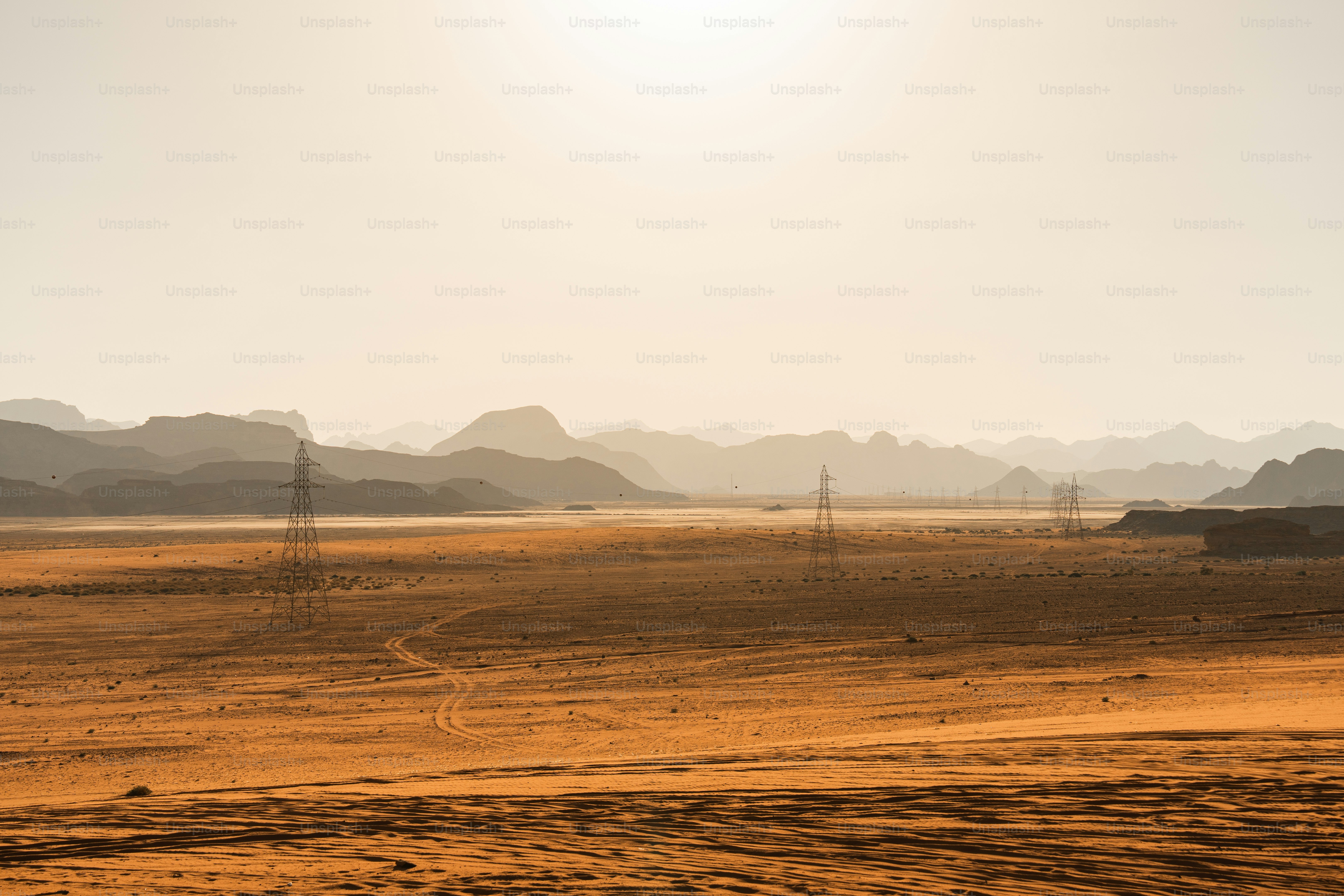 Electricity pylons in a vast desert landscape under a hazy golden sky