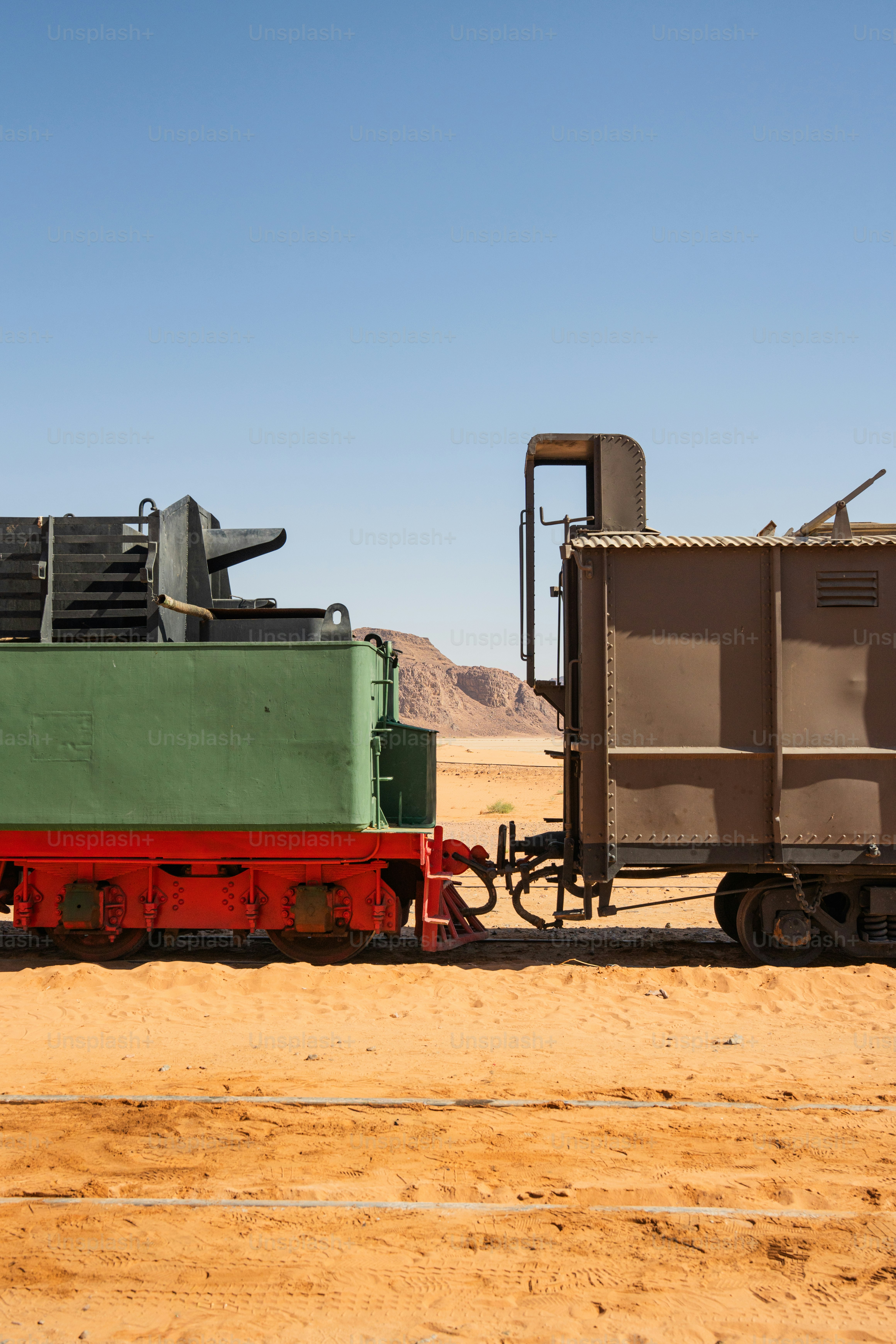 A green and red steam locomotive tender coupled to a brown train car in Rashidiyah