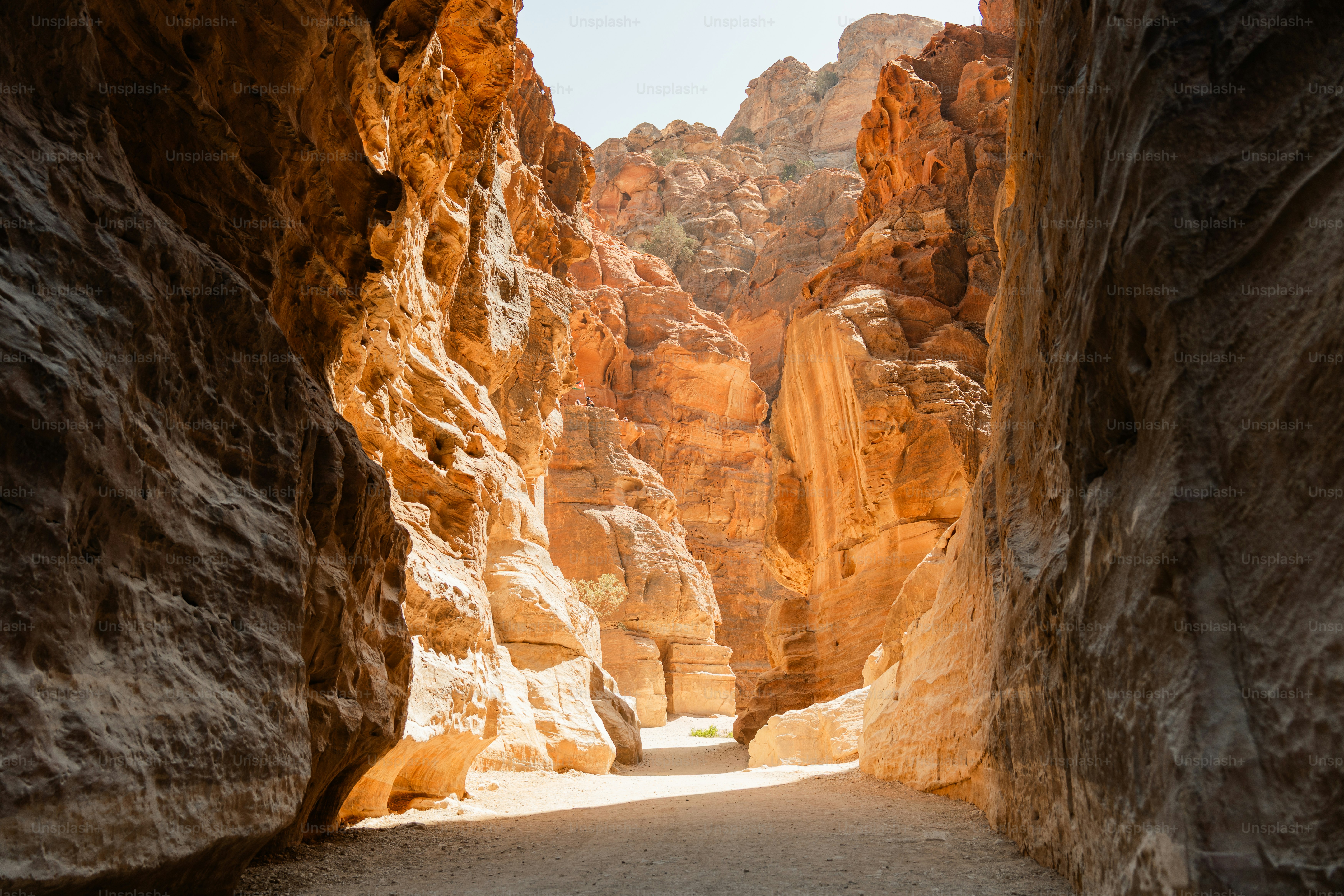 A narrow sandy path between towering orange sandstone cliffs in Wadi Musa, Jordan