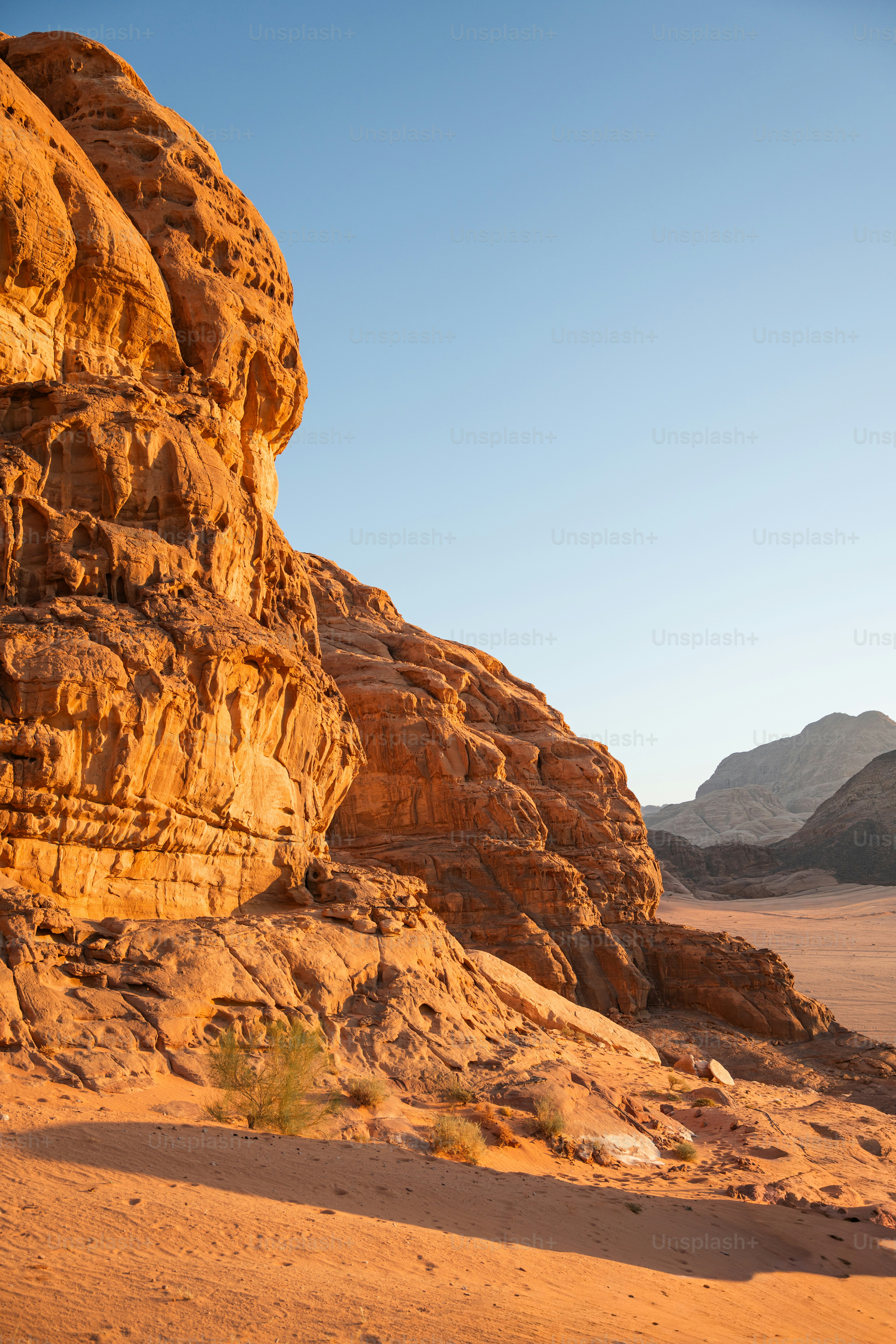 Orange sandstone cliffs rising above a sandy desert floor in Wadi Rum, Jordan