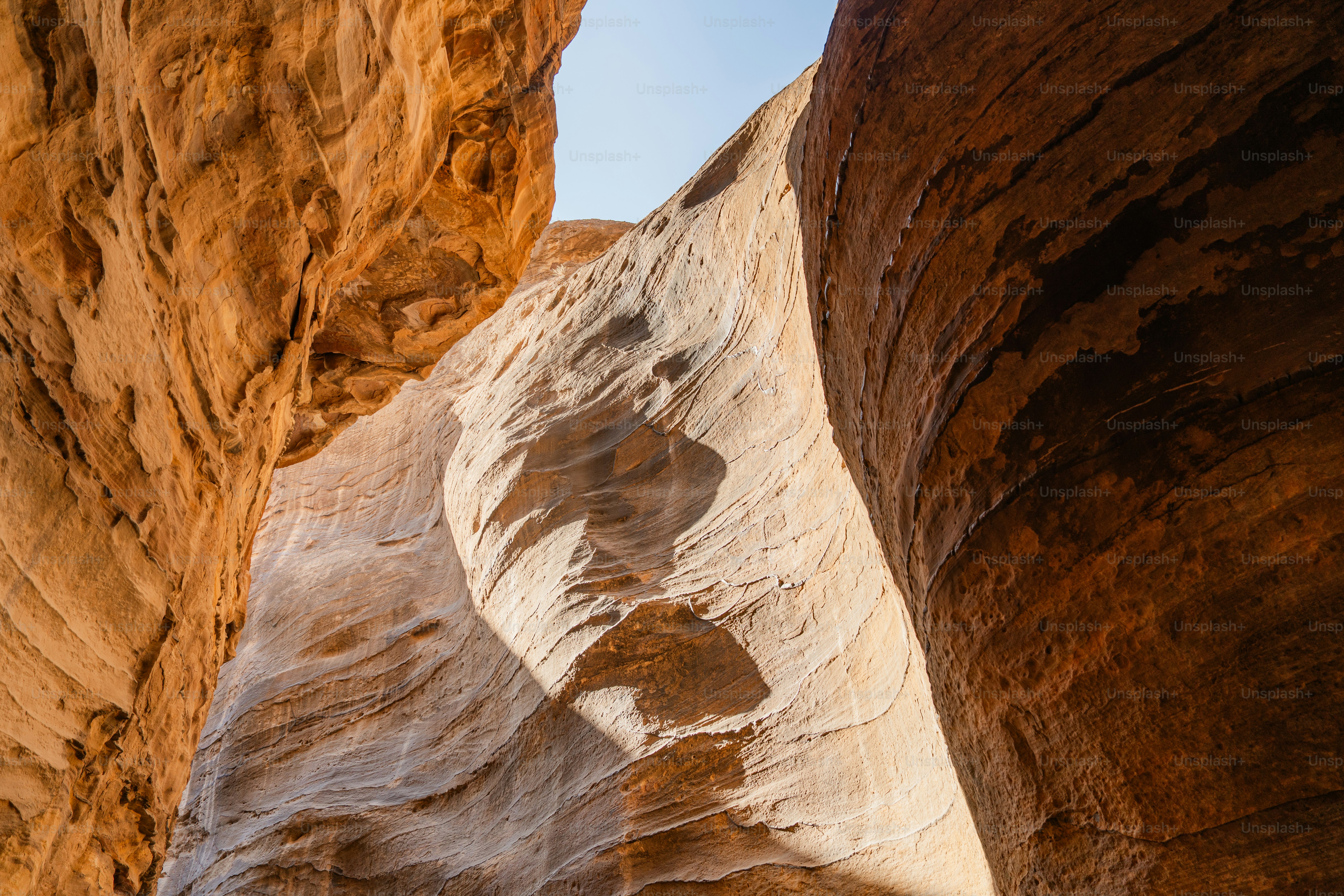 Tall orange sandstone canyon walls in Wadi Musa with a narrow strip of blue sky
