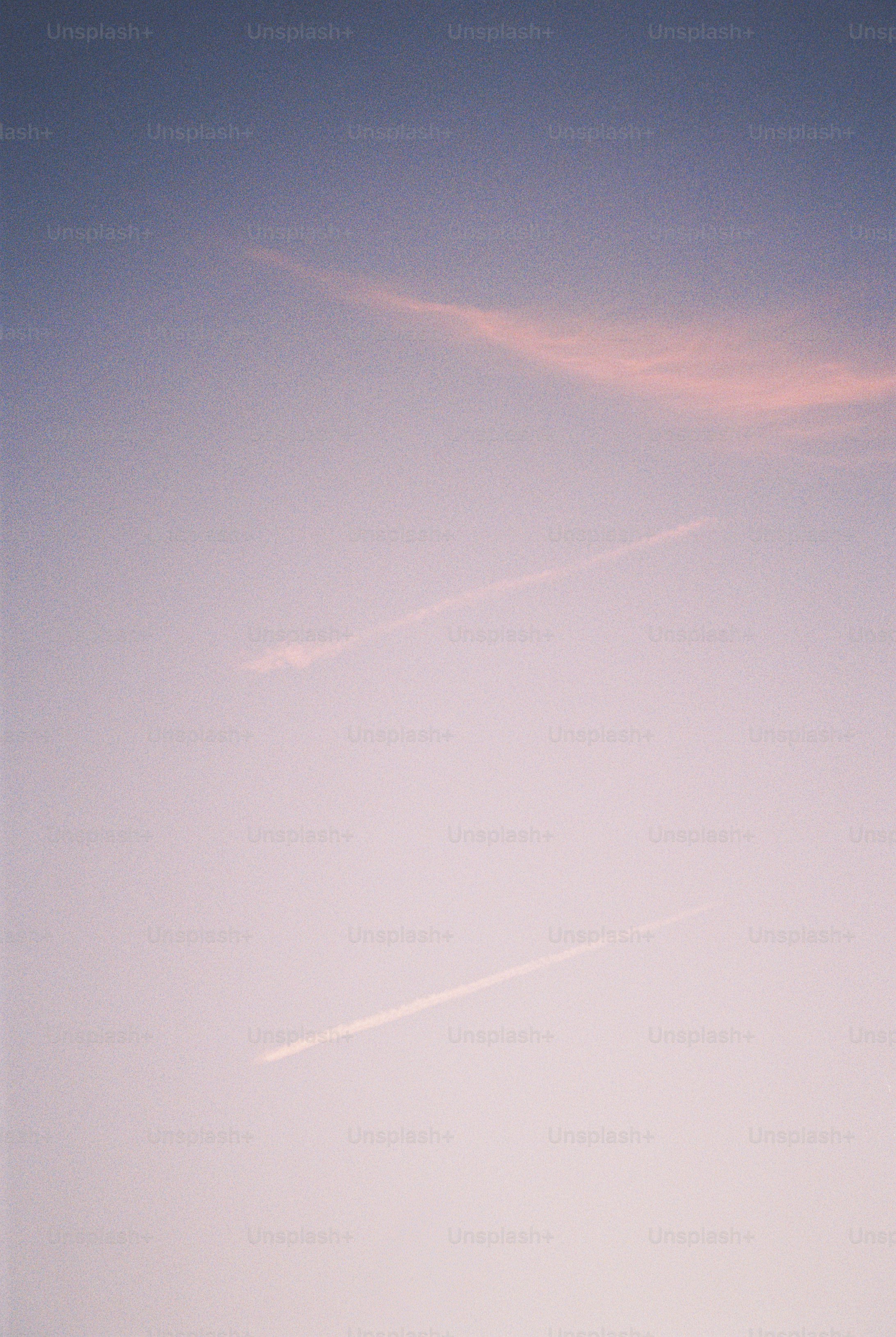 Two thin white contrails stretching across a soft purple and pink sky