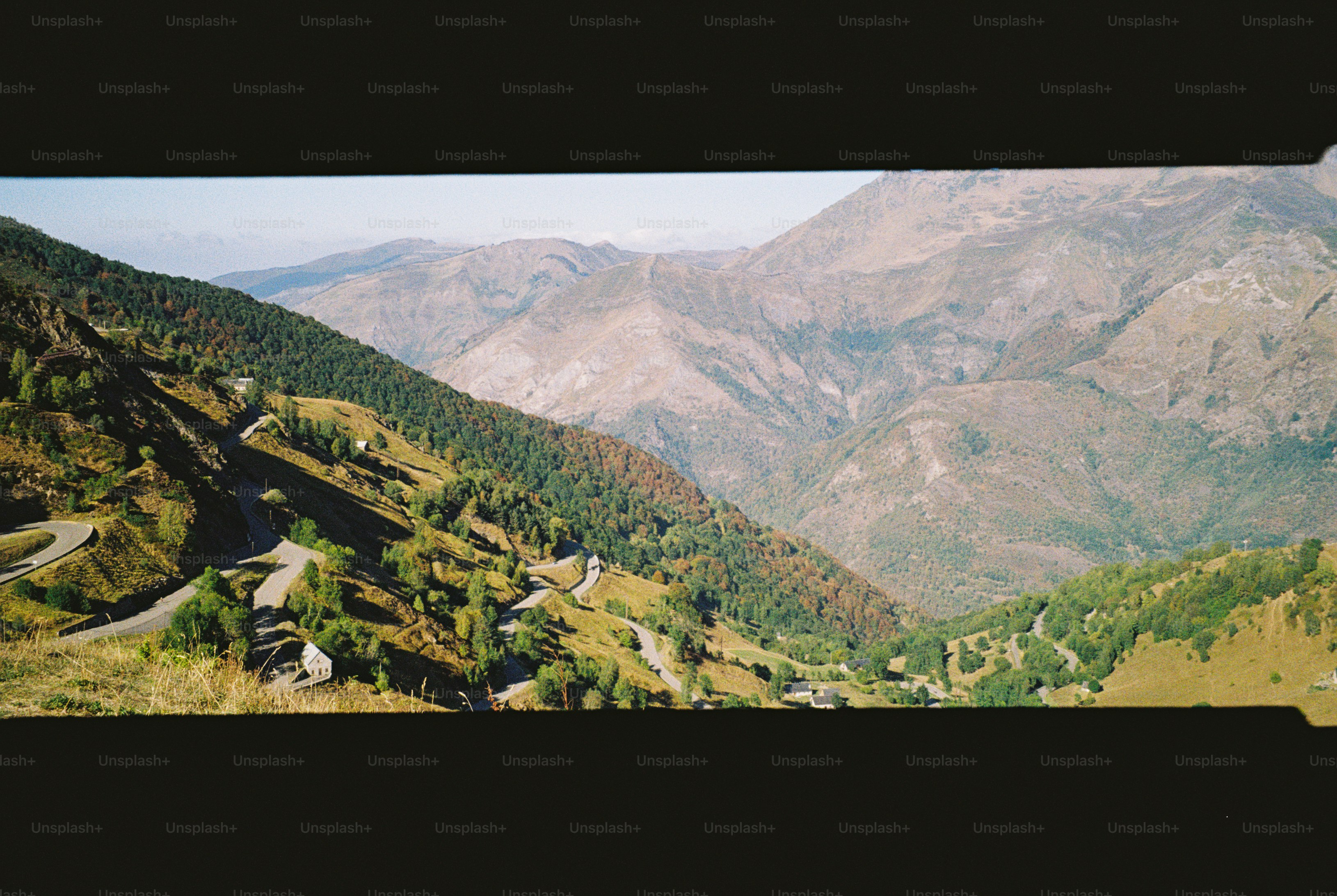 A winding road through a green mountain valley with forested slopes and peaks