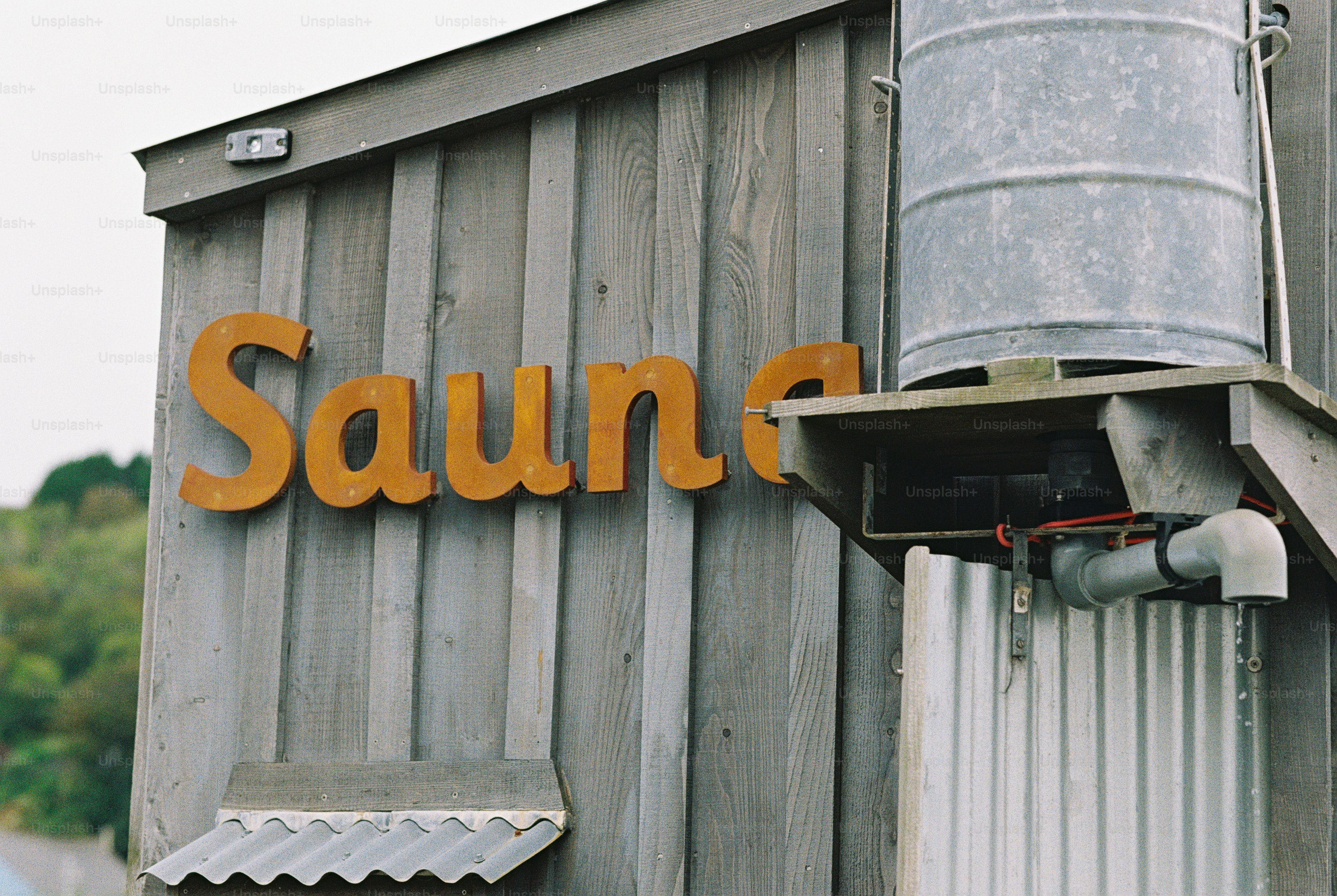 A rusted metal sign reading Sauna on a grey wooden wall with a water tank