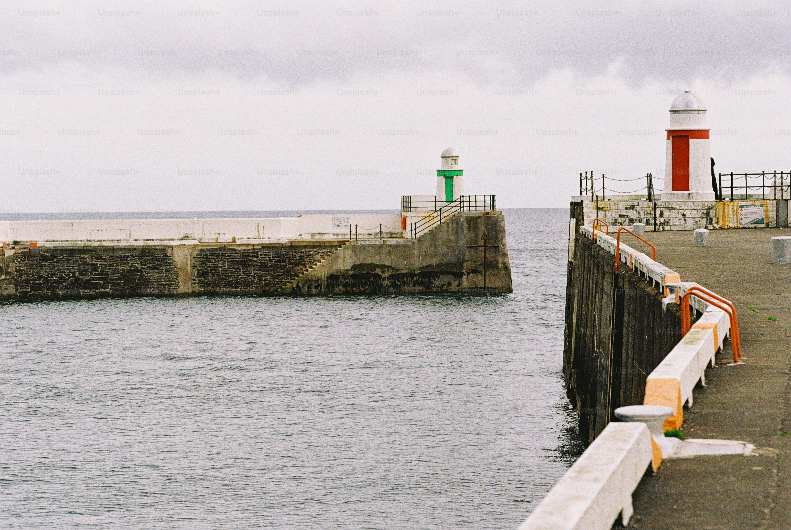 Two stone harbor piers with small lighthouses extending into the sea under a cloudy sky