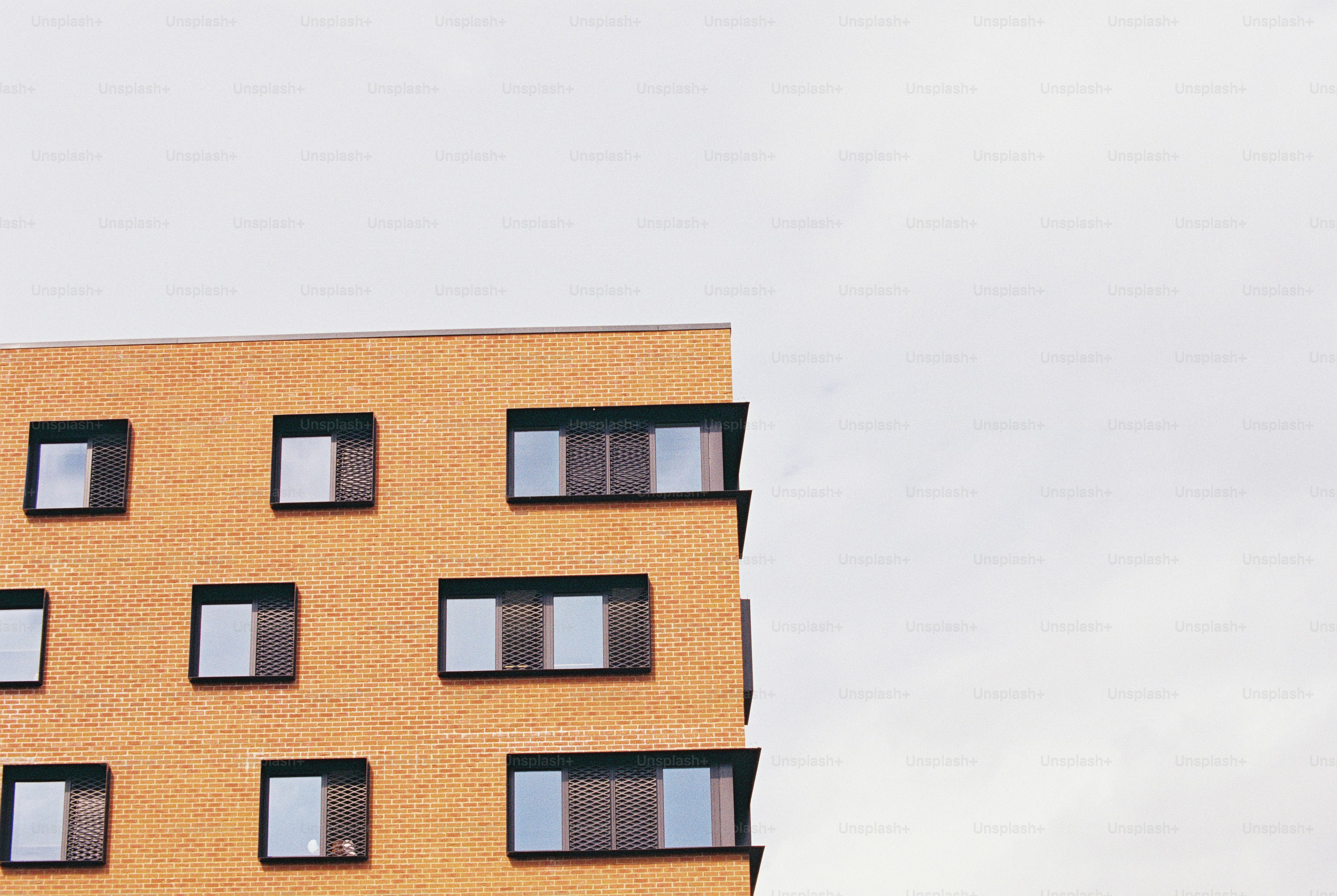 The corner of an orange brick building with dark framed windows and mesh shutters
