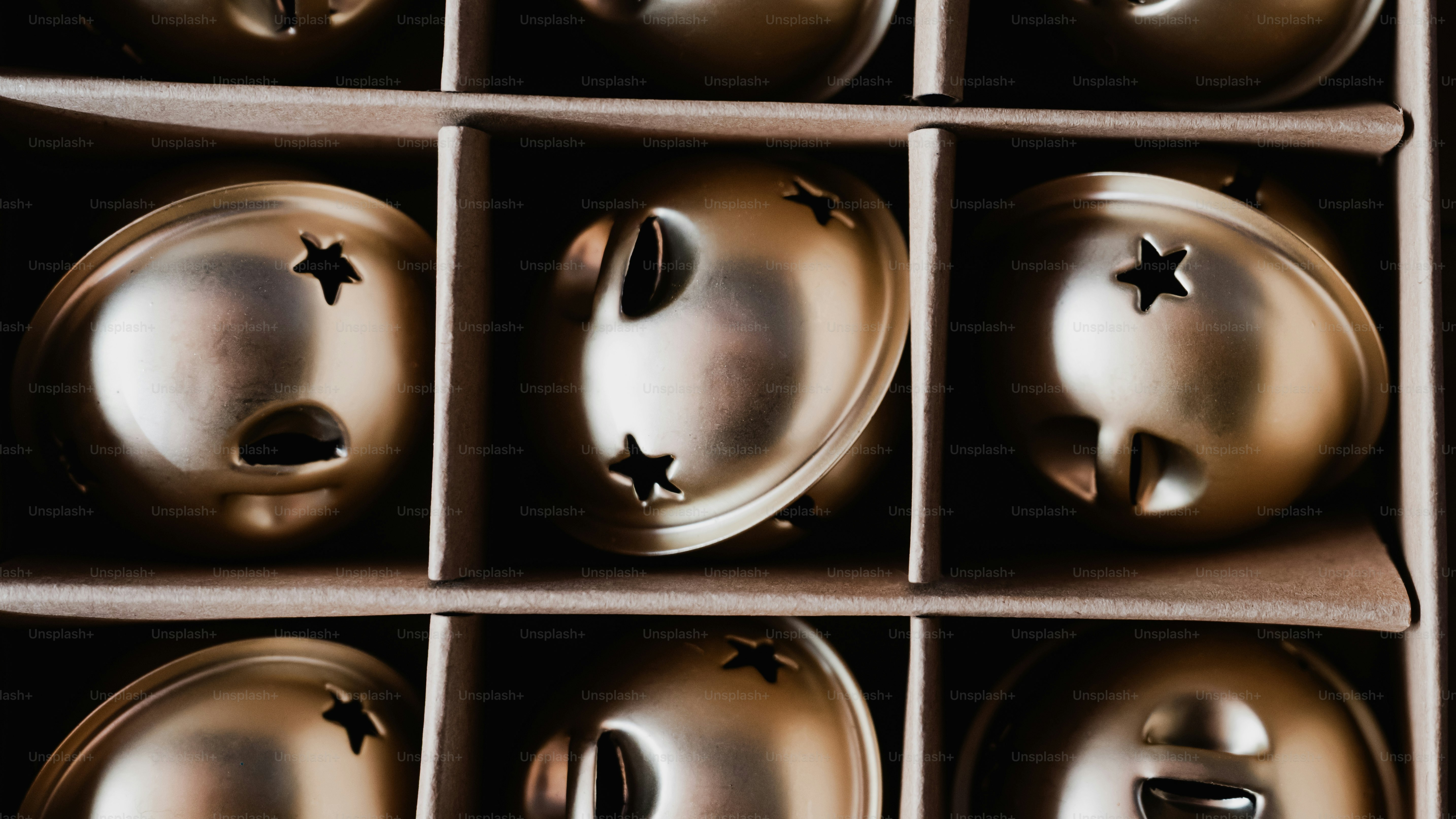 Gold jingle bells with star cutouts arranged in a cardboard grid