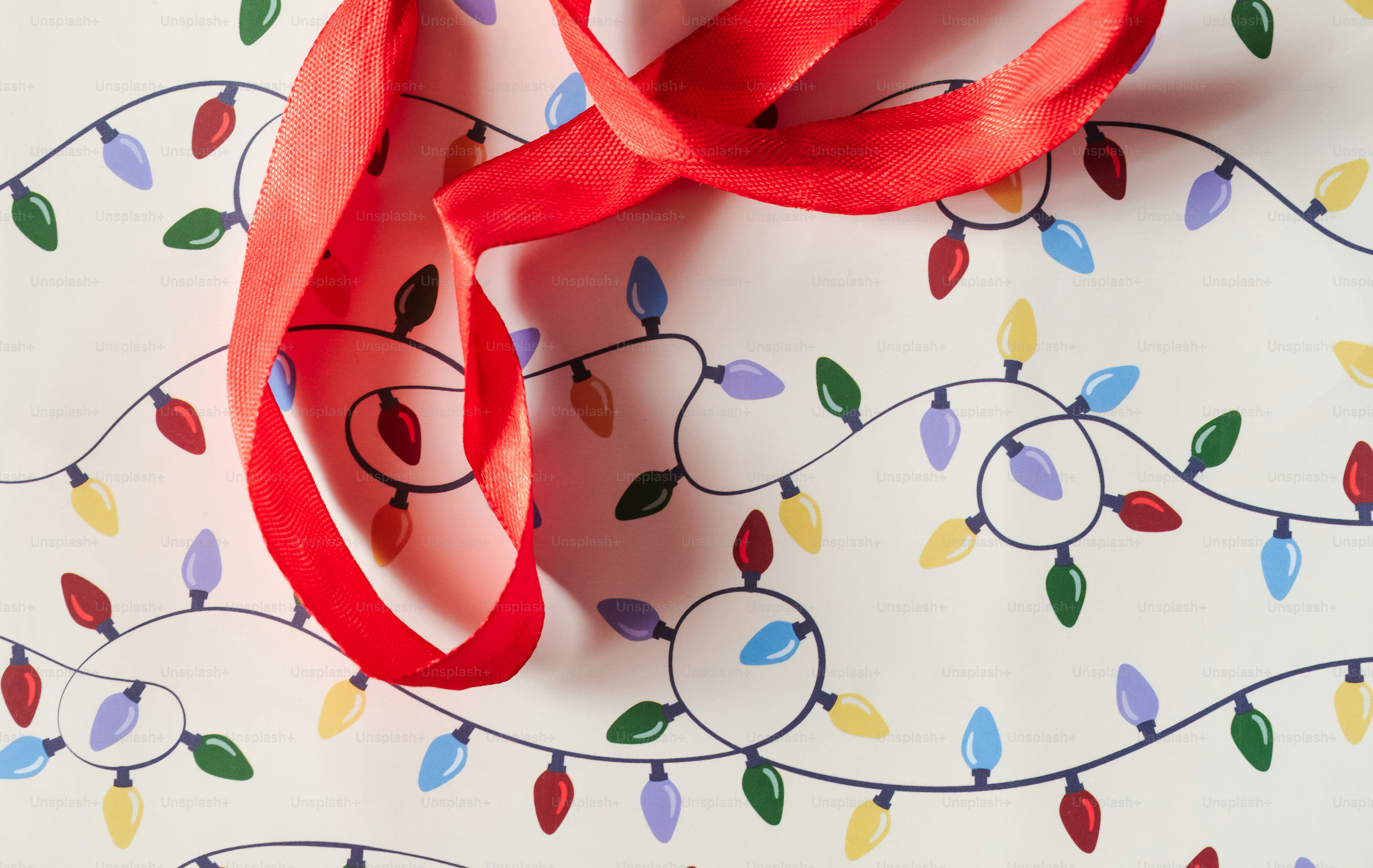A red ribbon draped over white wrapping paper patterned with colorful Christmas lights