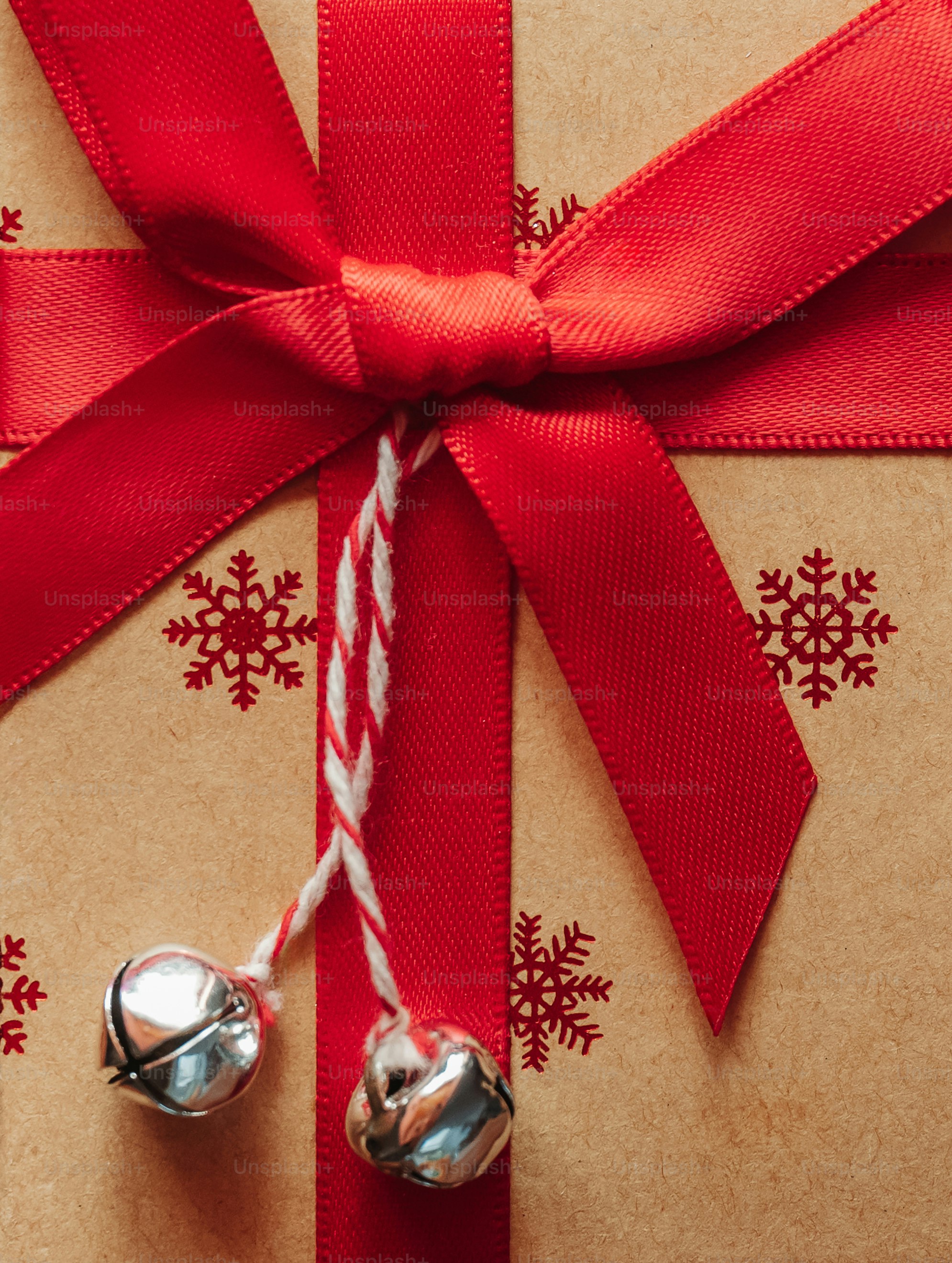A brown gift box with red snowflake patterns, a red ribbon, and silver bells
