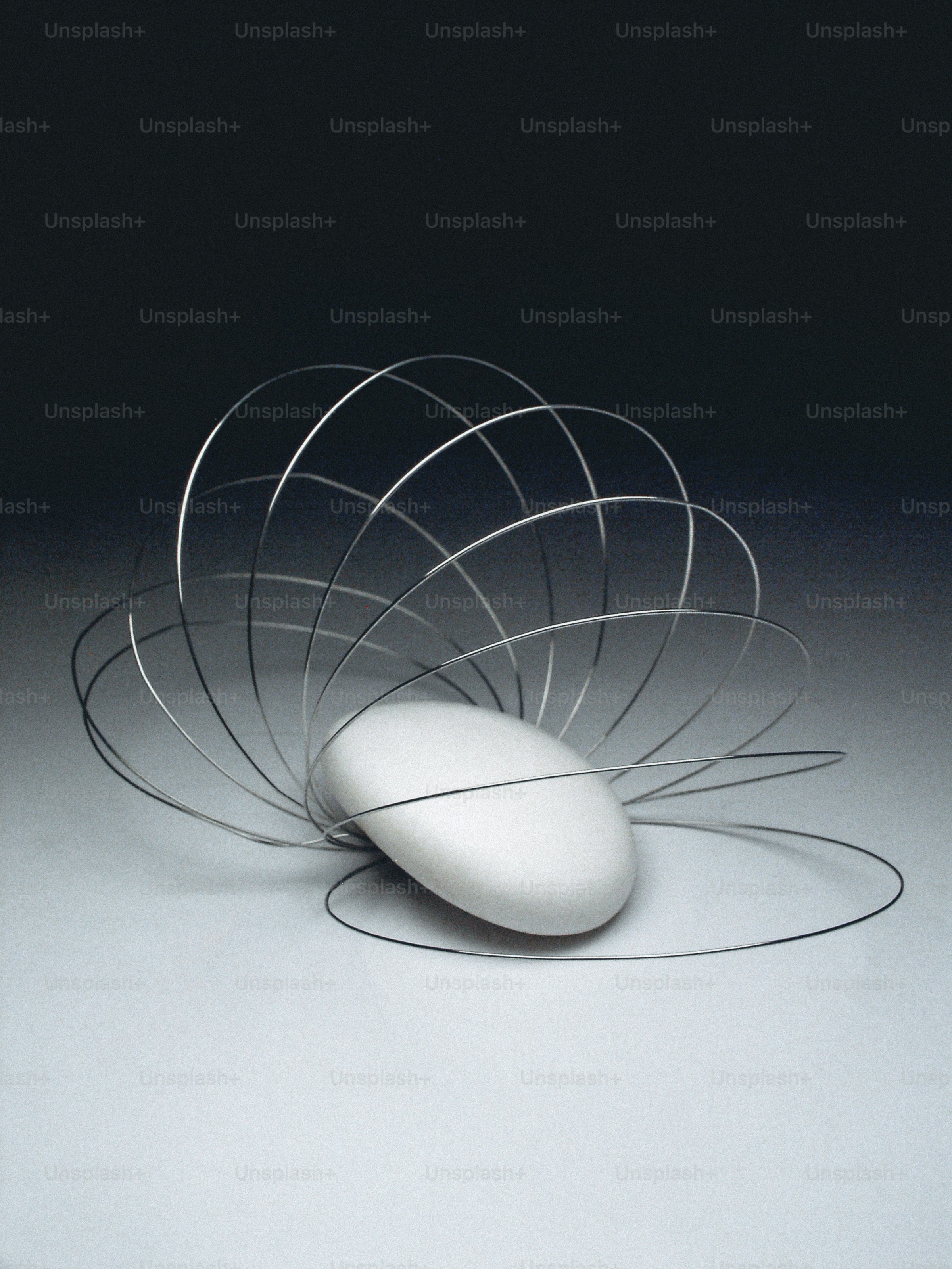 A smooth white stone surrounded by thin metallic wire loops on a grey surface