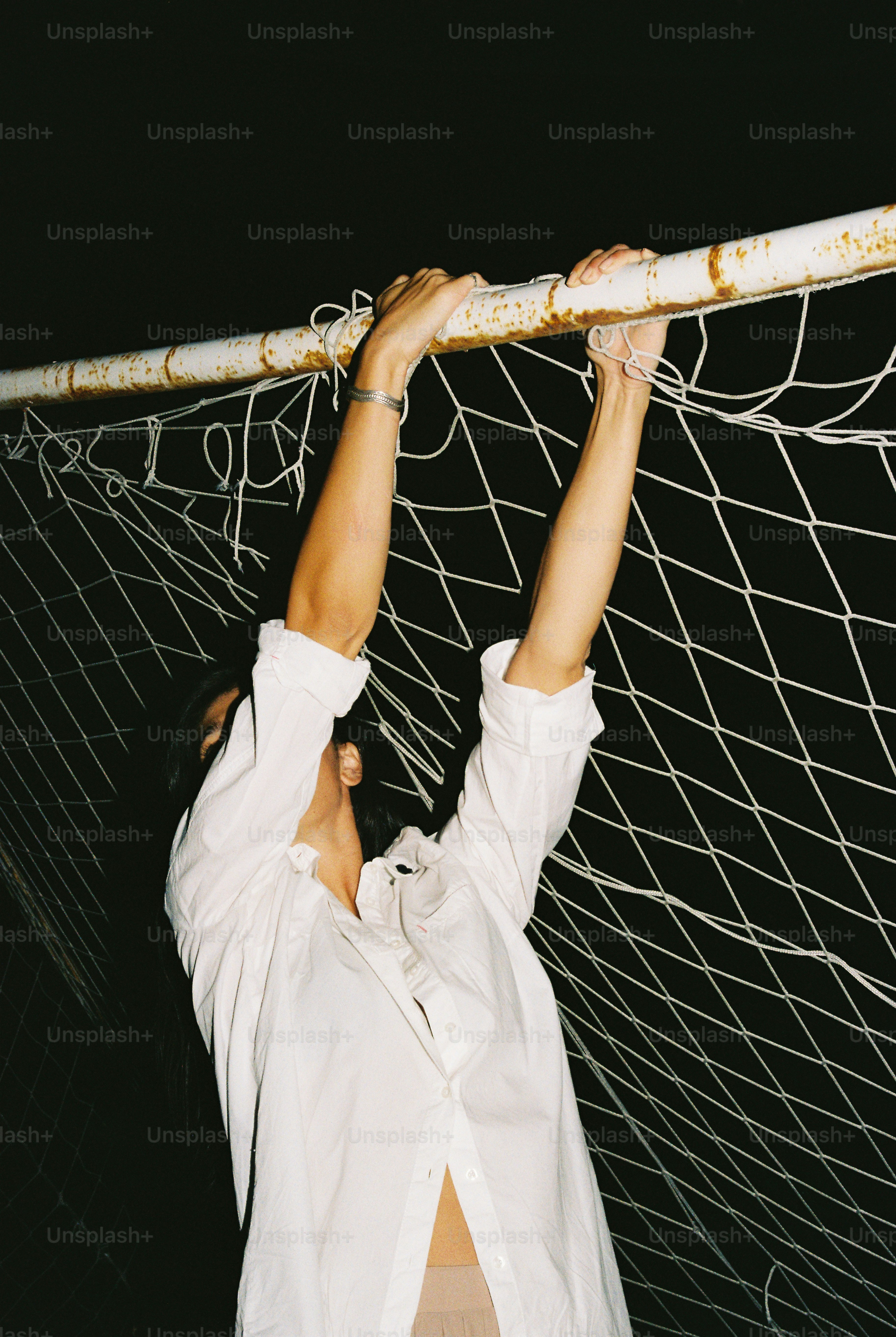 A person in a white shirt hanging from a rusted soccer goal net