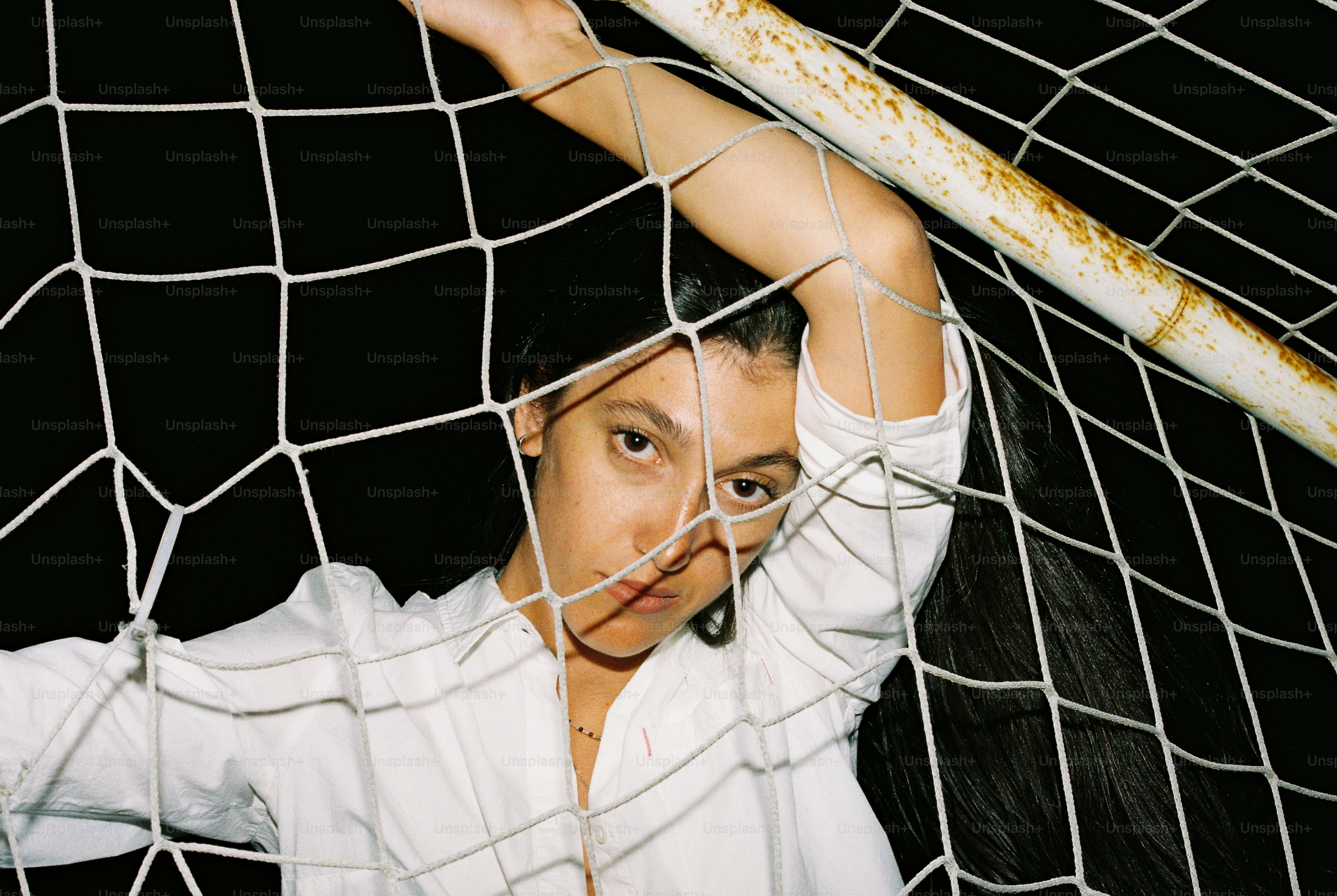 A woman in a white shirt behind a weathered soccer goal net