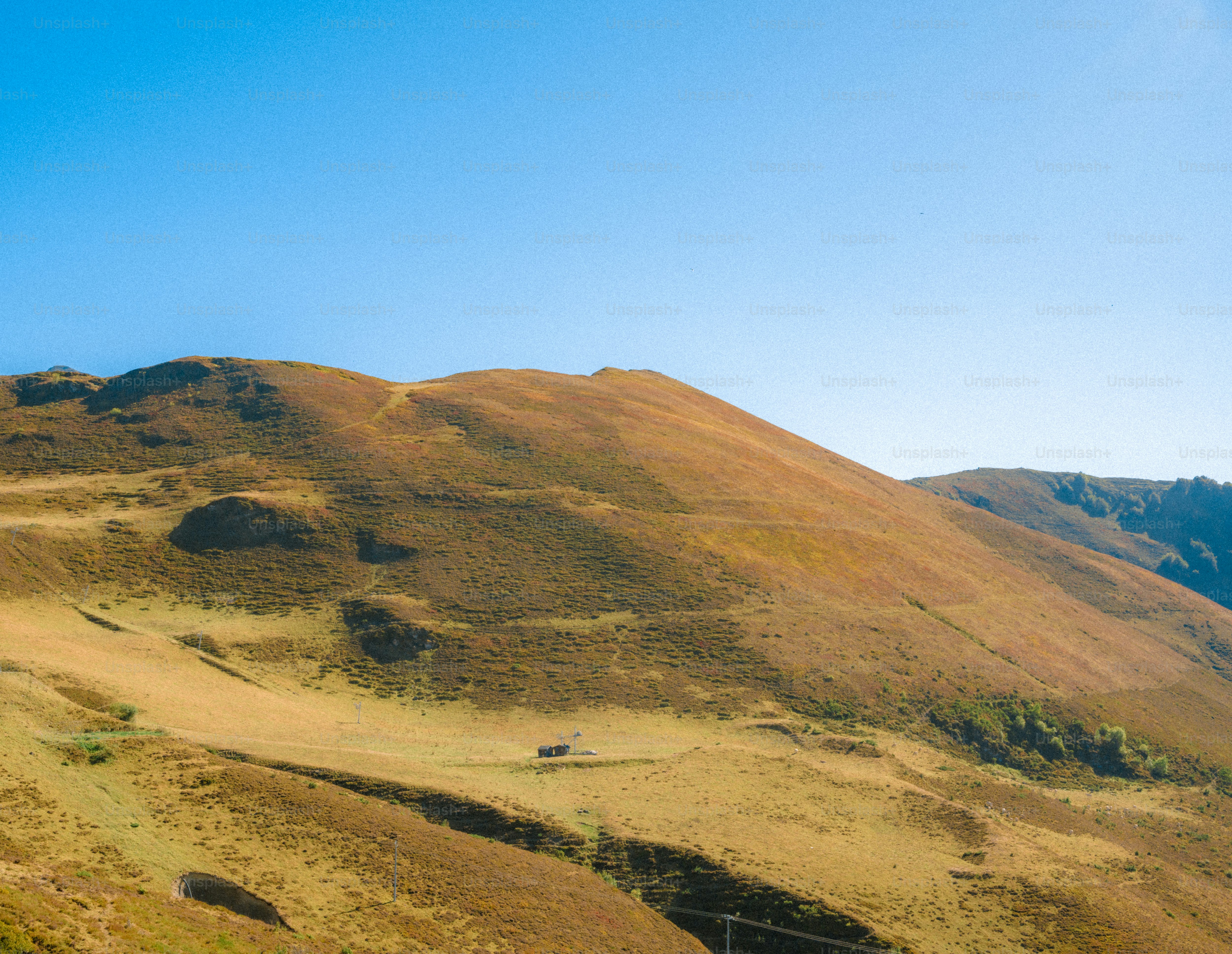 A small cabin on a vast golden hillside under a clear blue sky