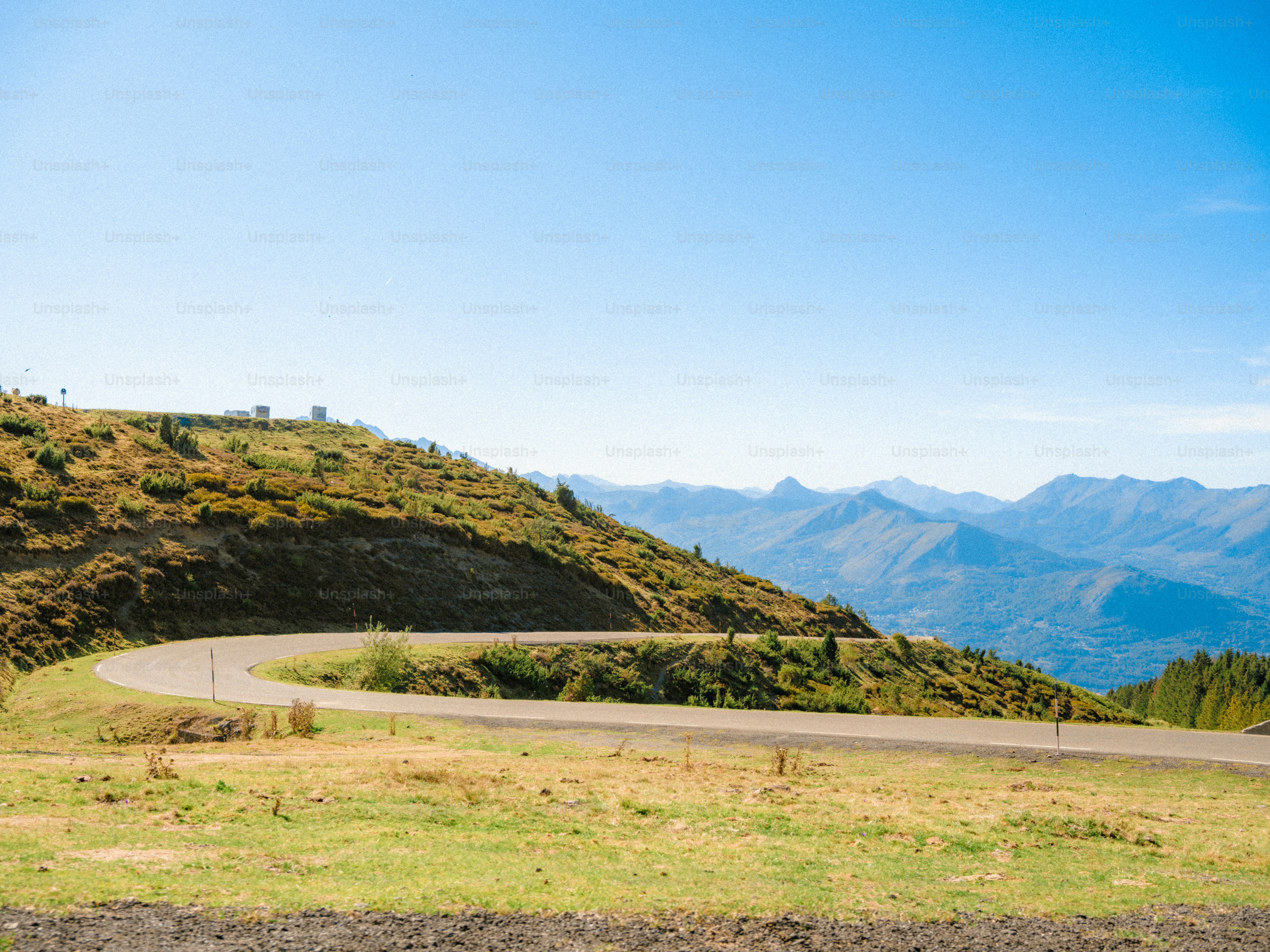 A winding asphalt road curving through a grassy mountain landscape under a clear sky