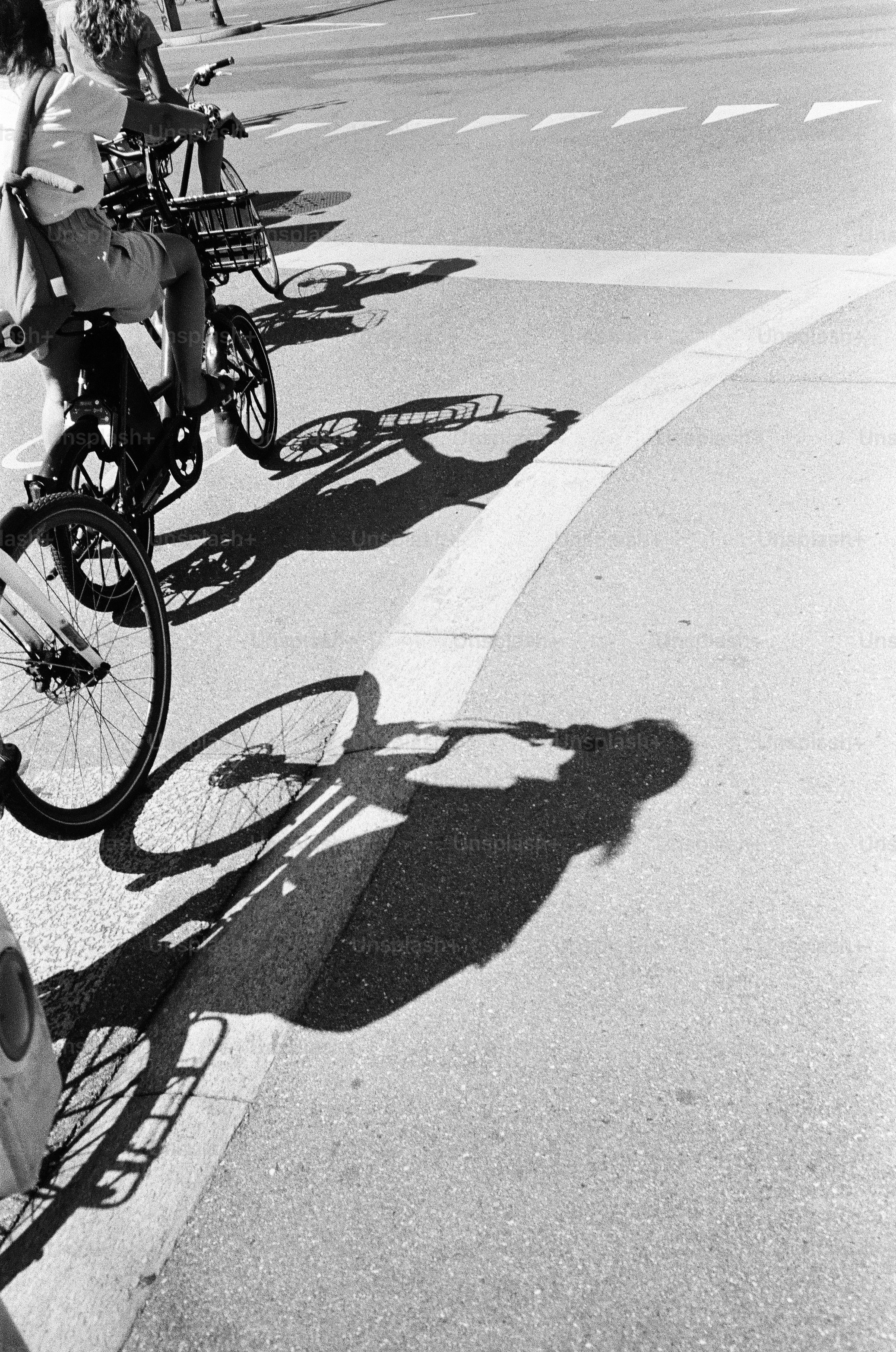 Two people cycling on a paved road with long shadows in black and white
