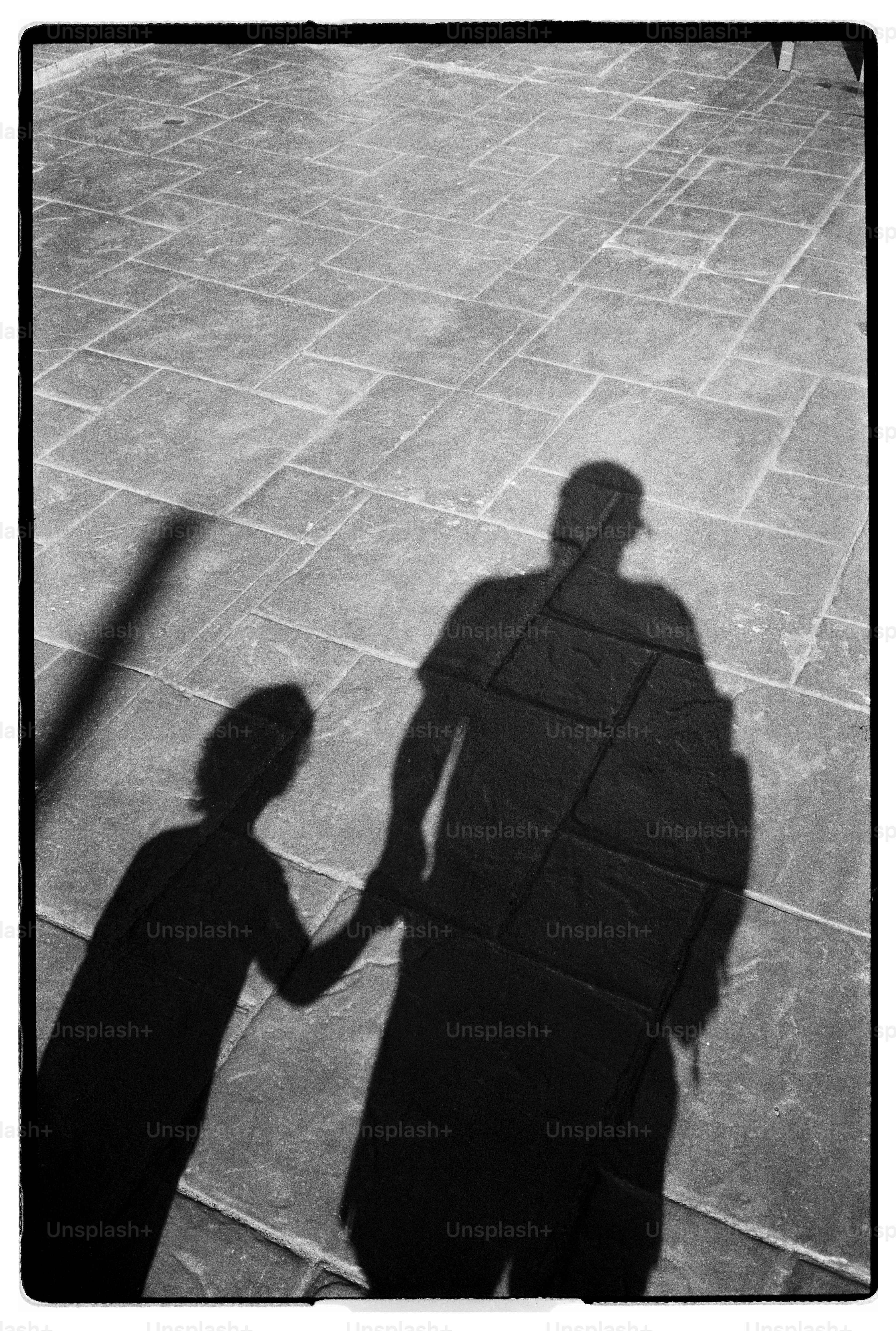 Shadow of an adult and a child holding hands on a stone patio