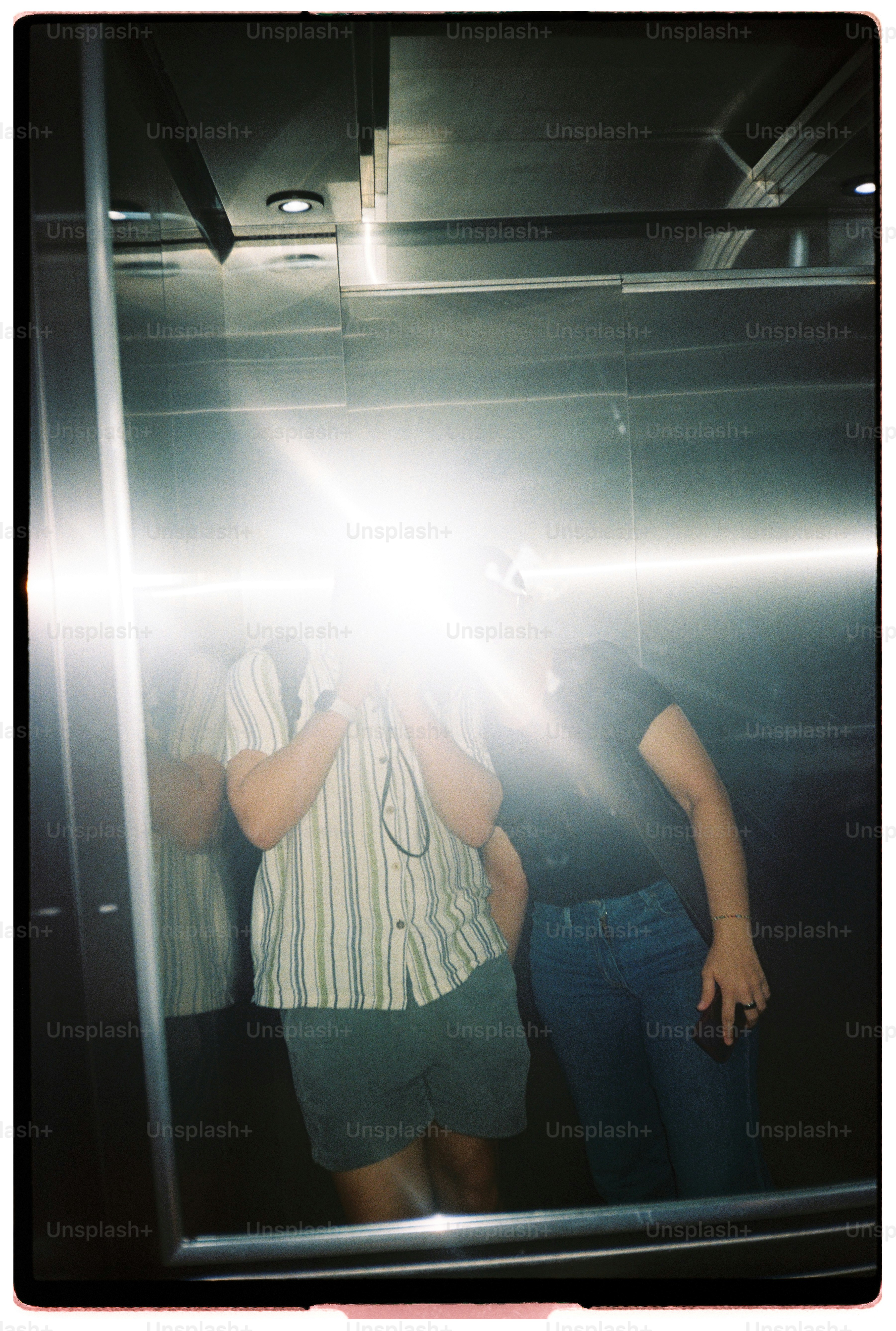 Two people reflected in a metal elevator mirror with a bright camera flash
