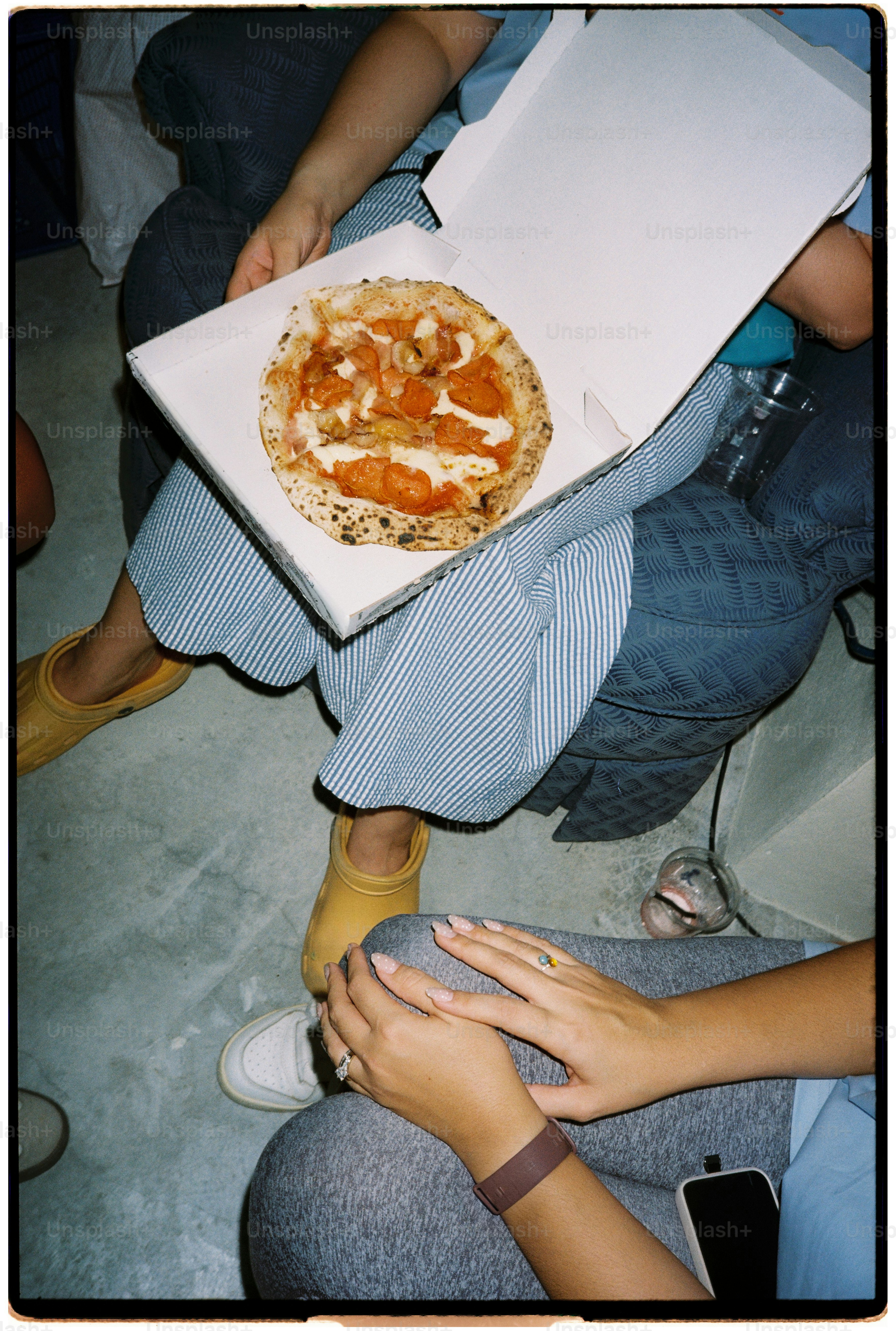 A person holding a pizza box with a small pizza on their lap