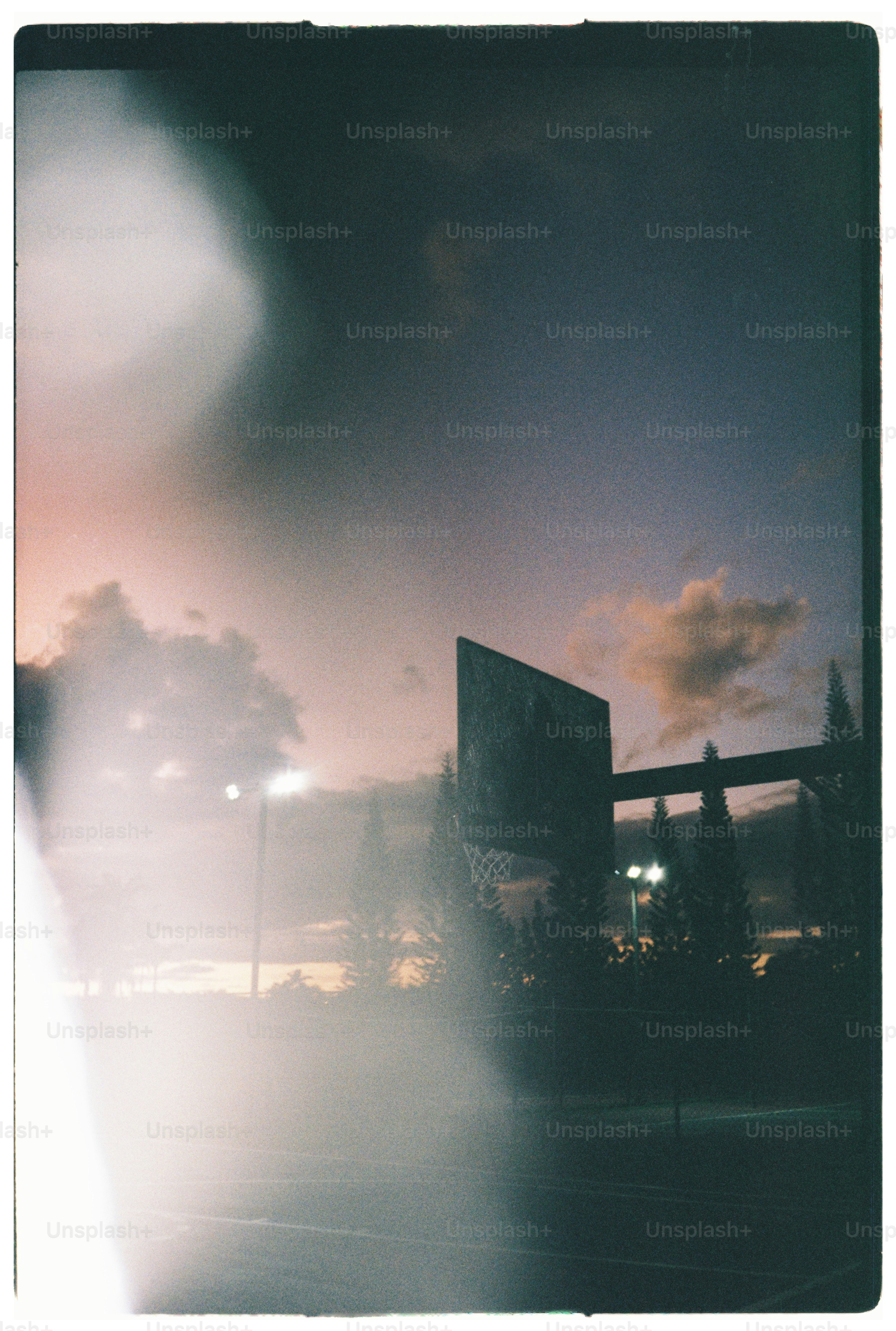 A basketball hoop silhouette against a warm sky with light flare
