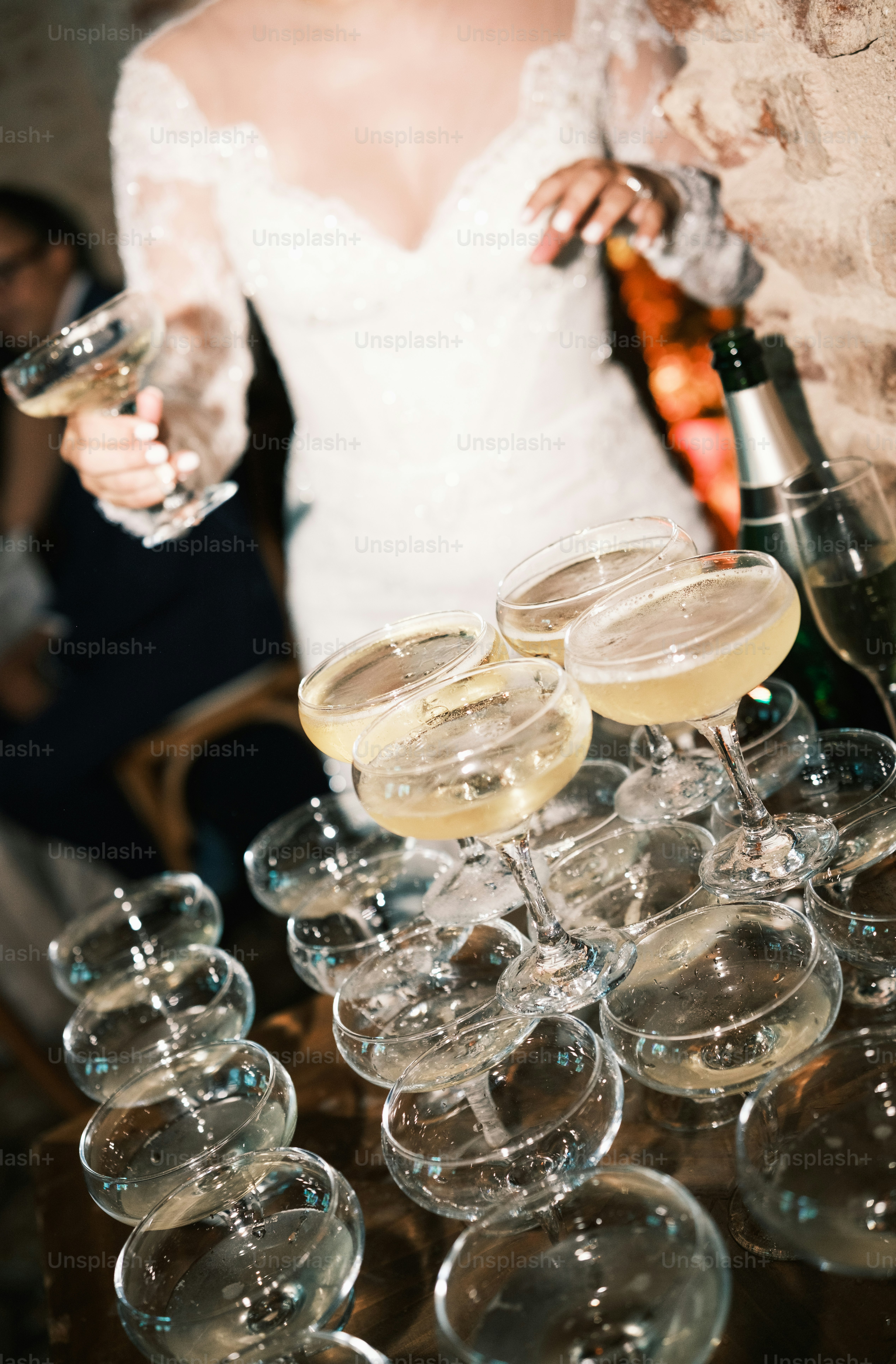 A person in a white lace dress holding a champagne coupe near a tower