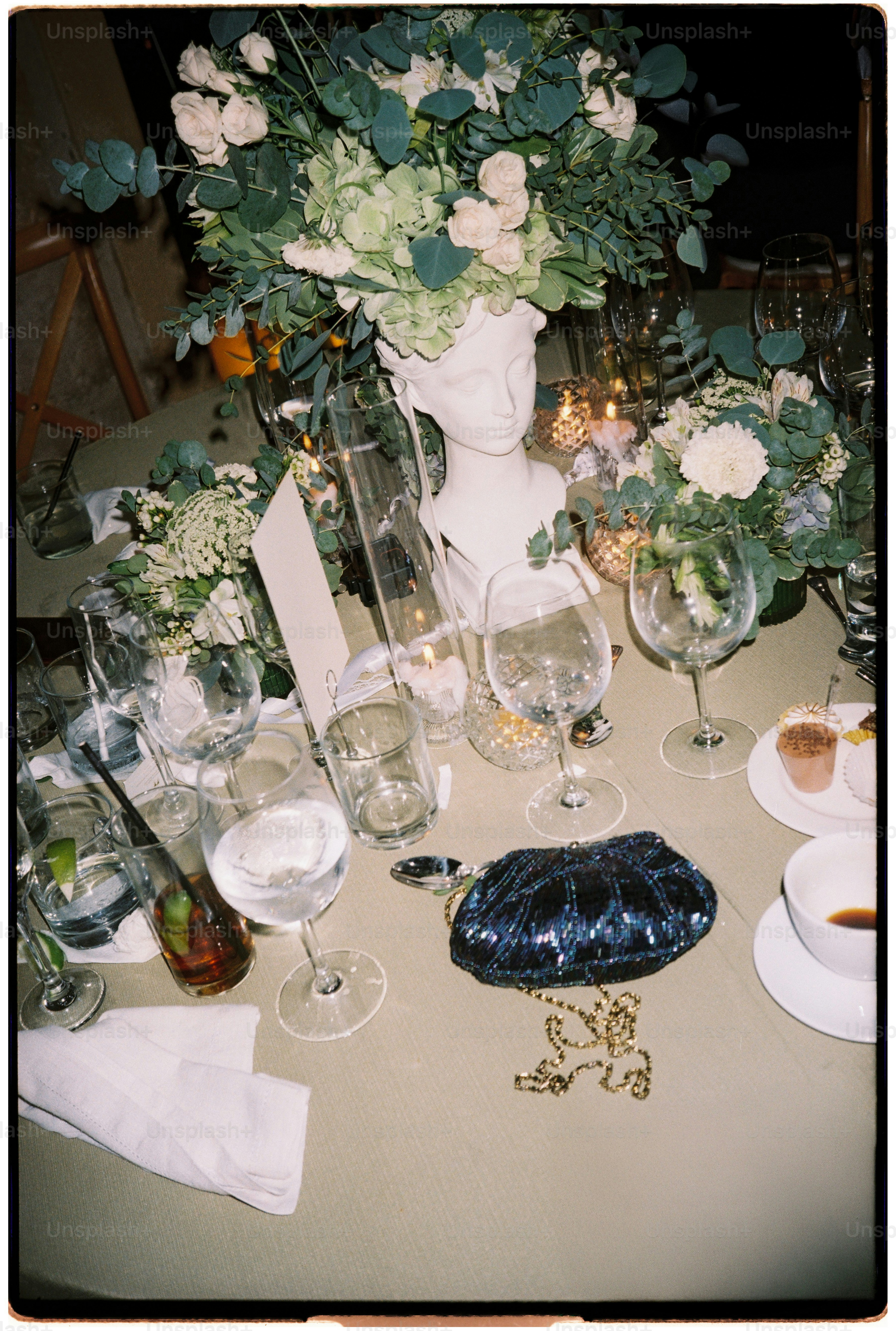 A table setting with a white bust vase, floral arrangements, wine glasses, and a clutch