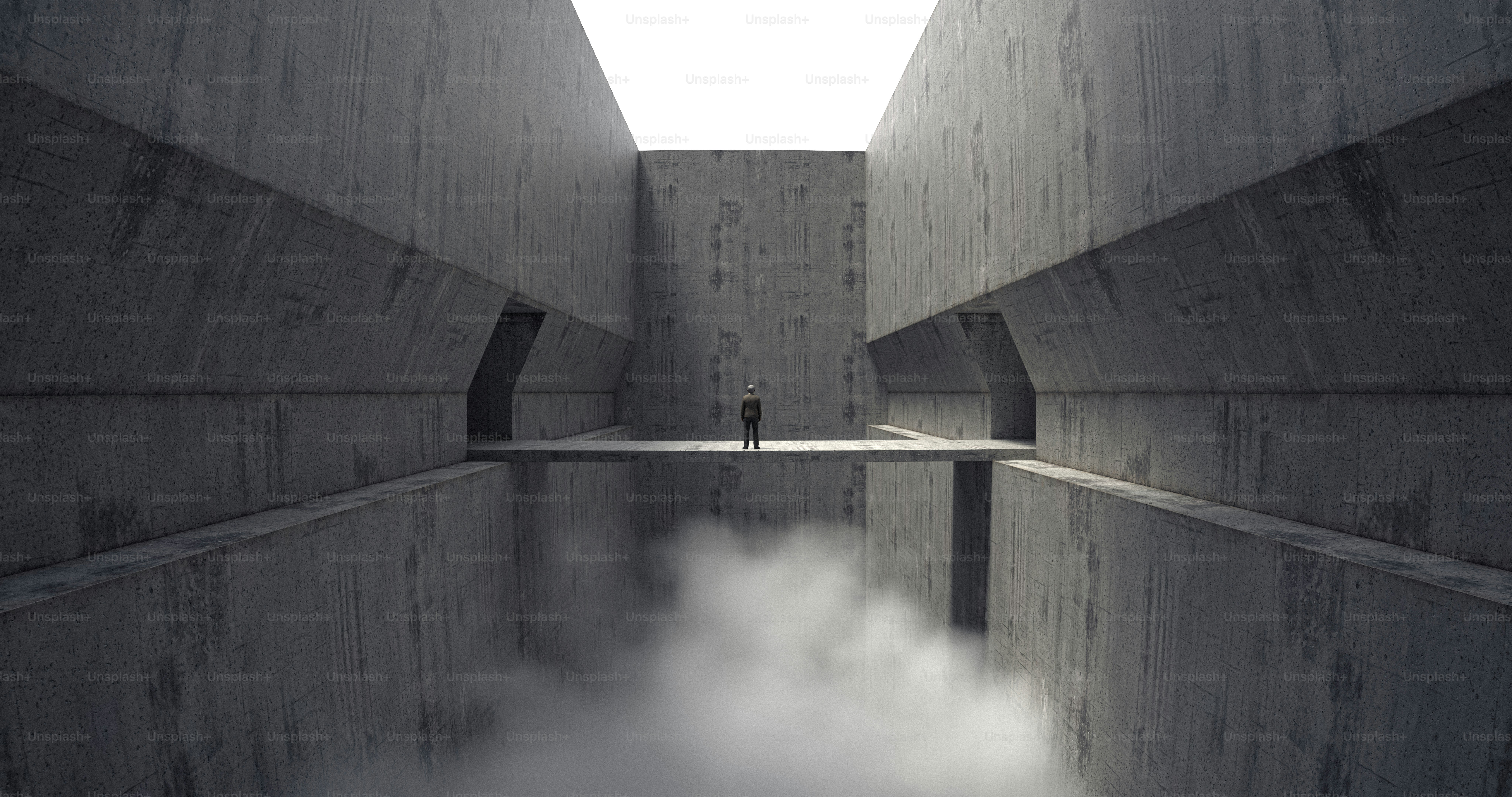 A person on a narrow concrete bridge between tall walls above thick fog