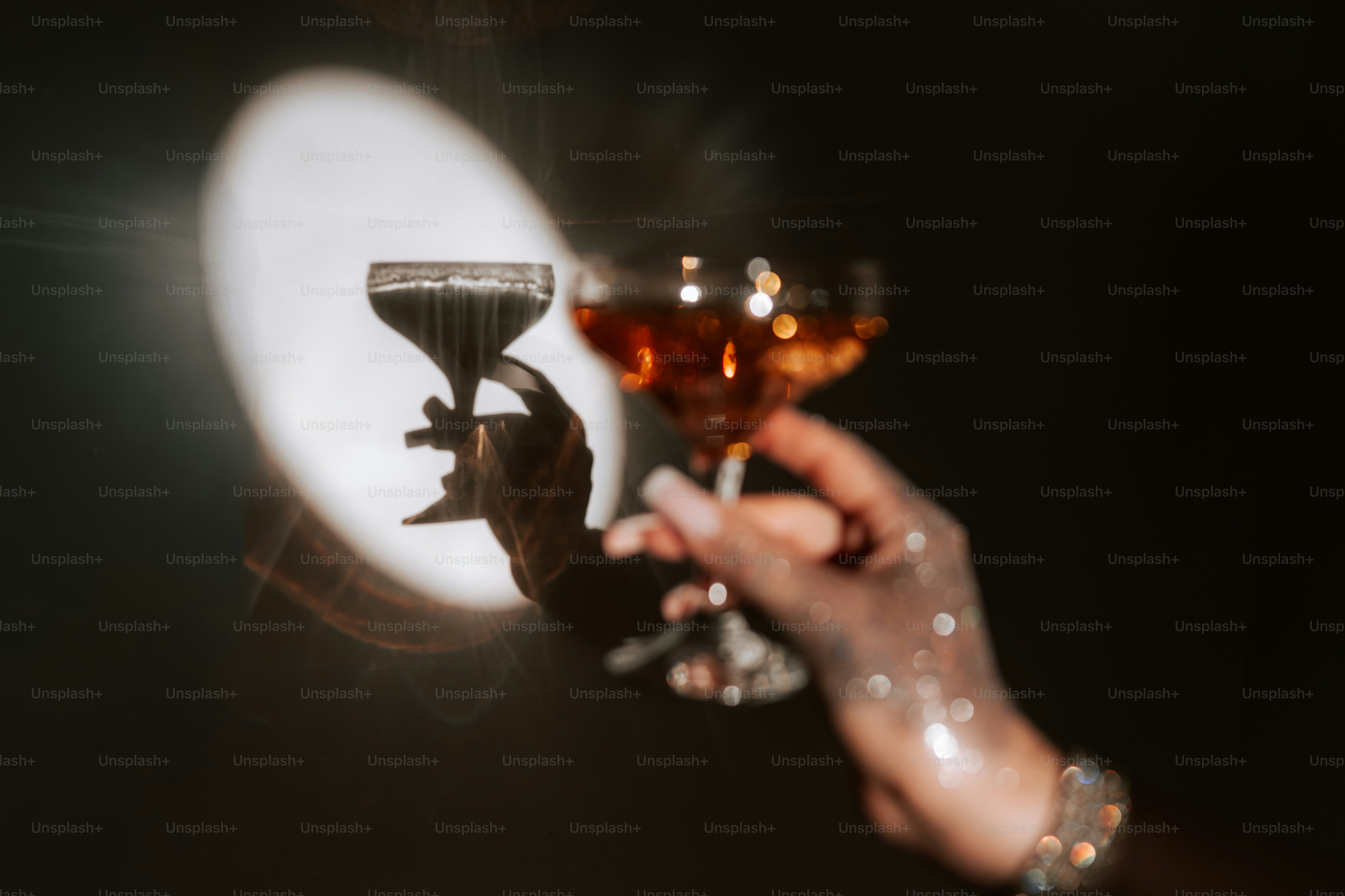 A hand holding a cocktail glass against a bright circular spotlight in darkness