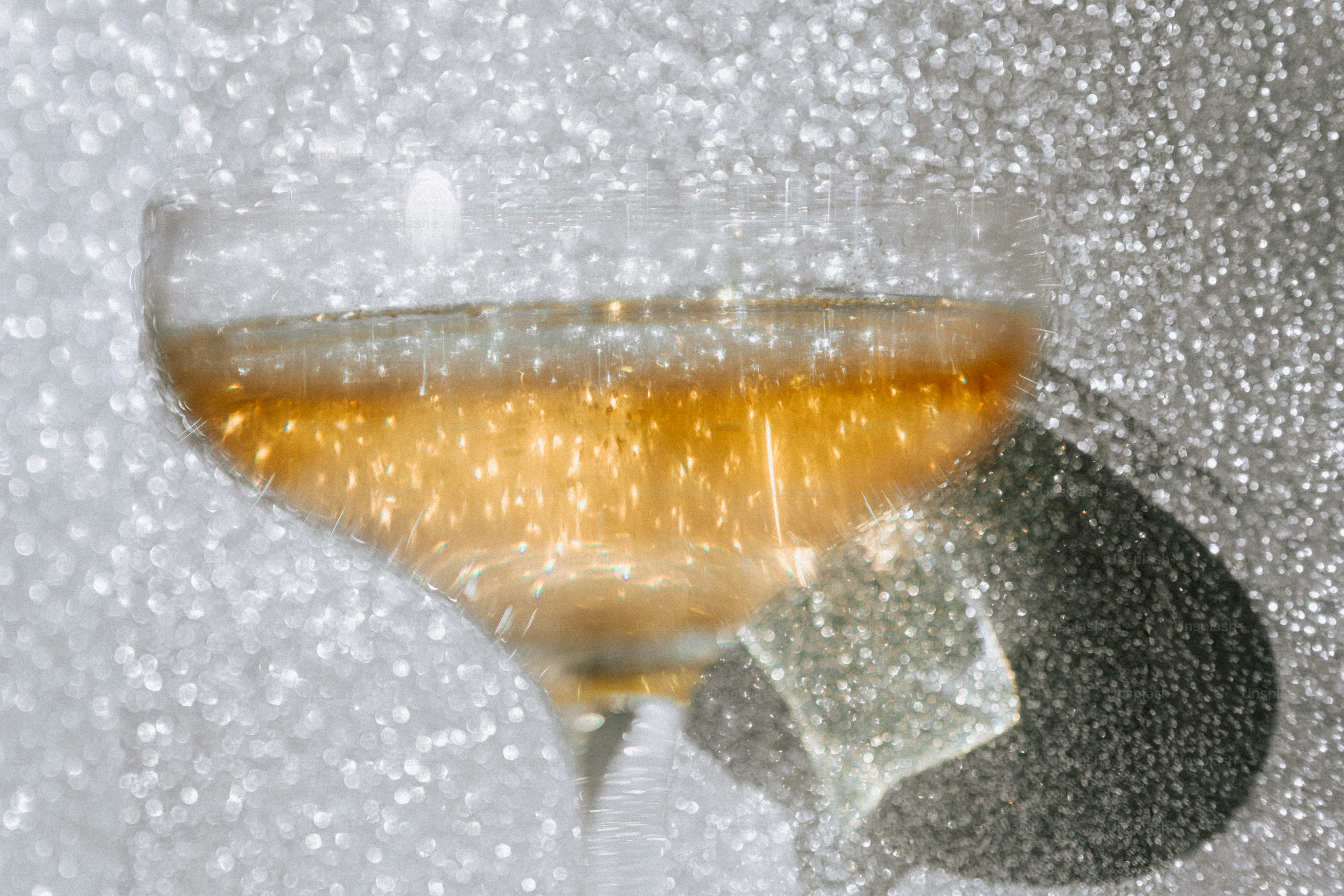 A coupe glass filled with golden liquid against a shimmering silver glitter background