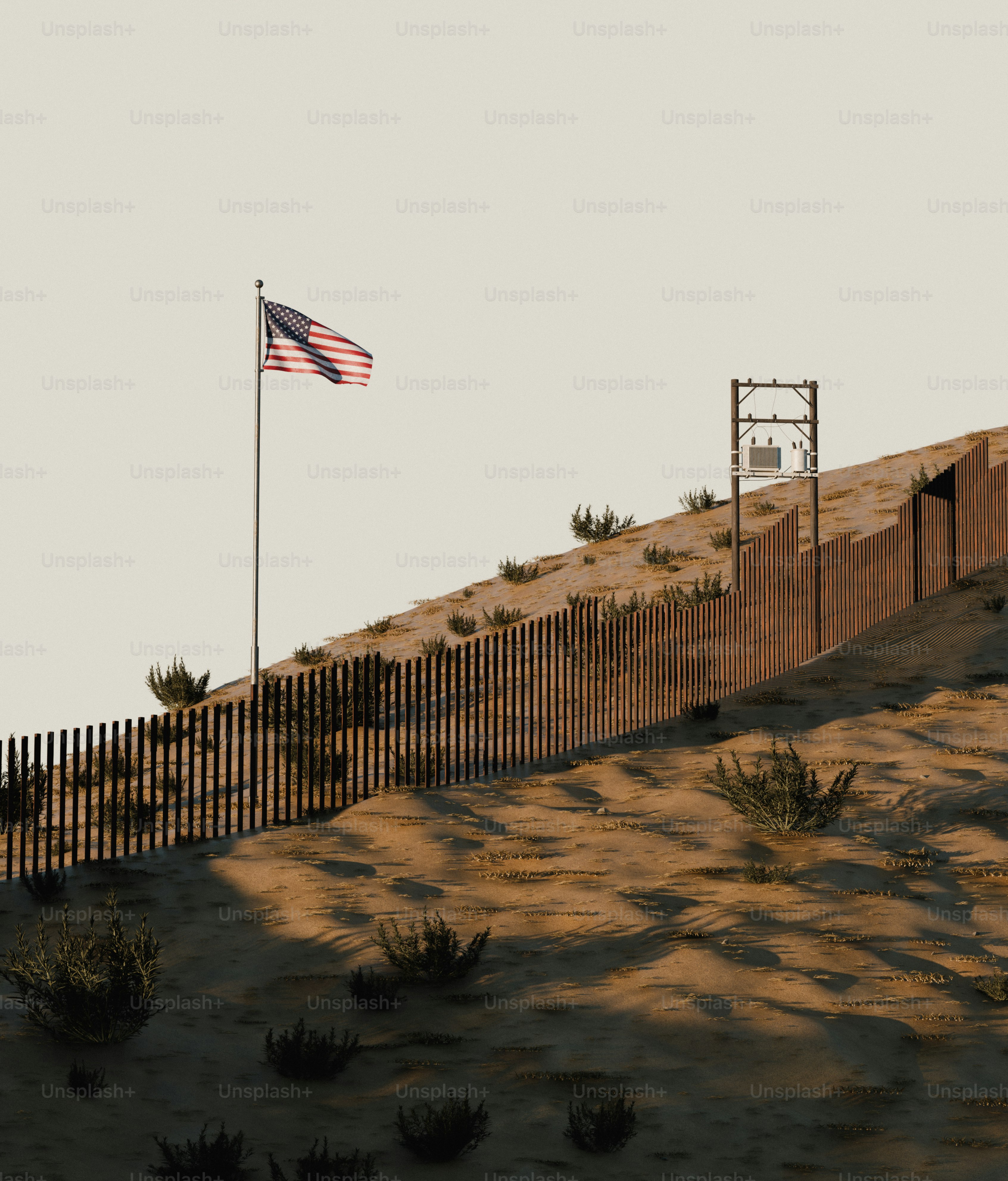 An American flag on a pole beside a border fence on a sandy hill