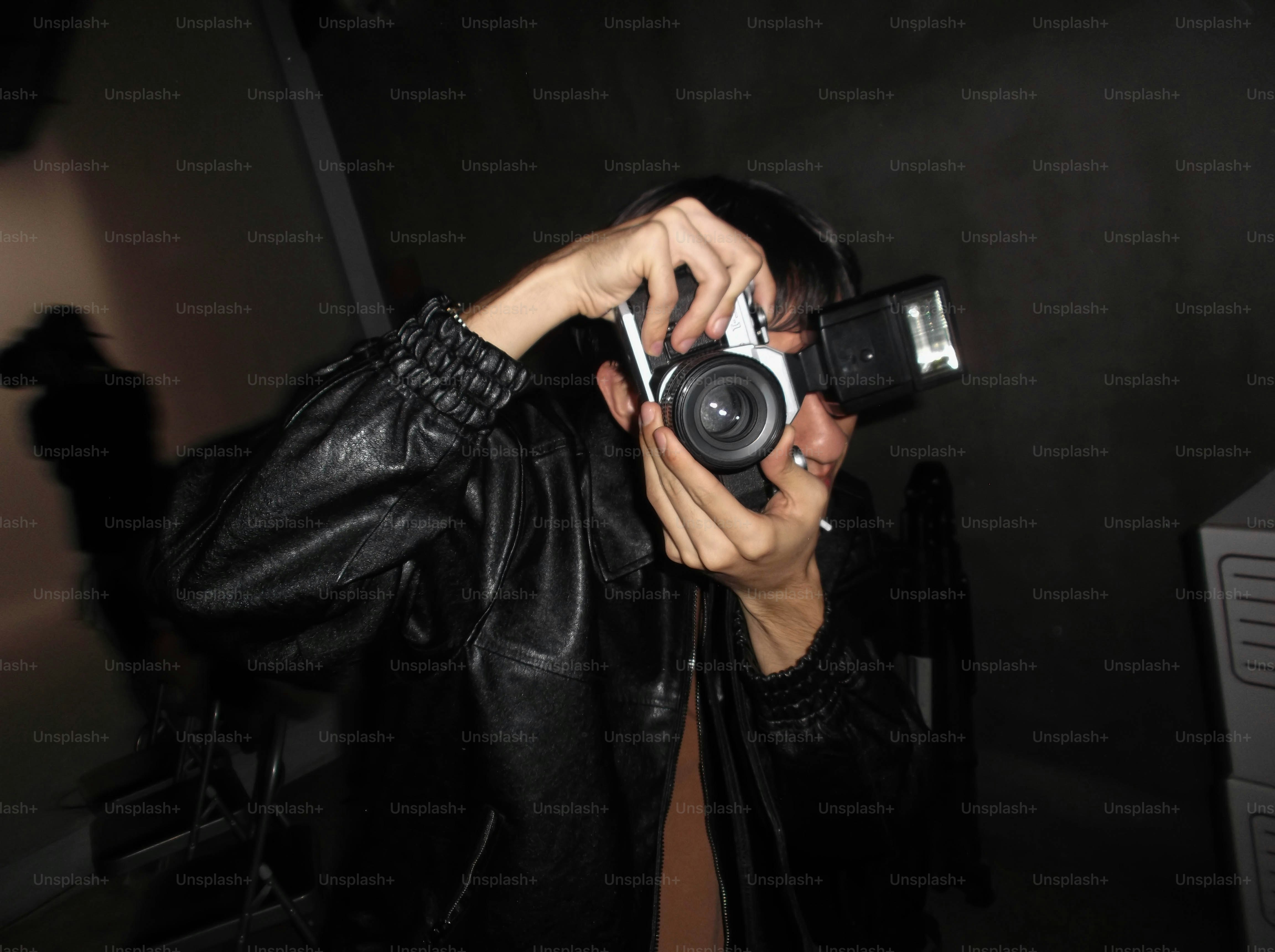 A person in a black leather jacket holding a camera with a flash