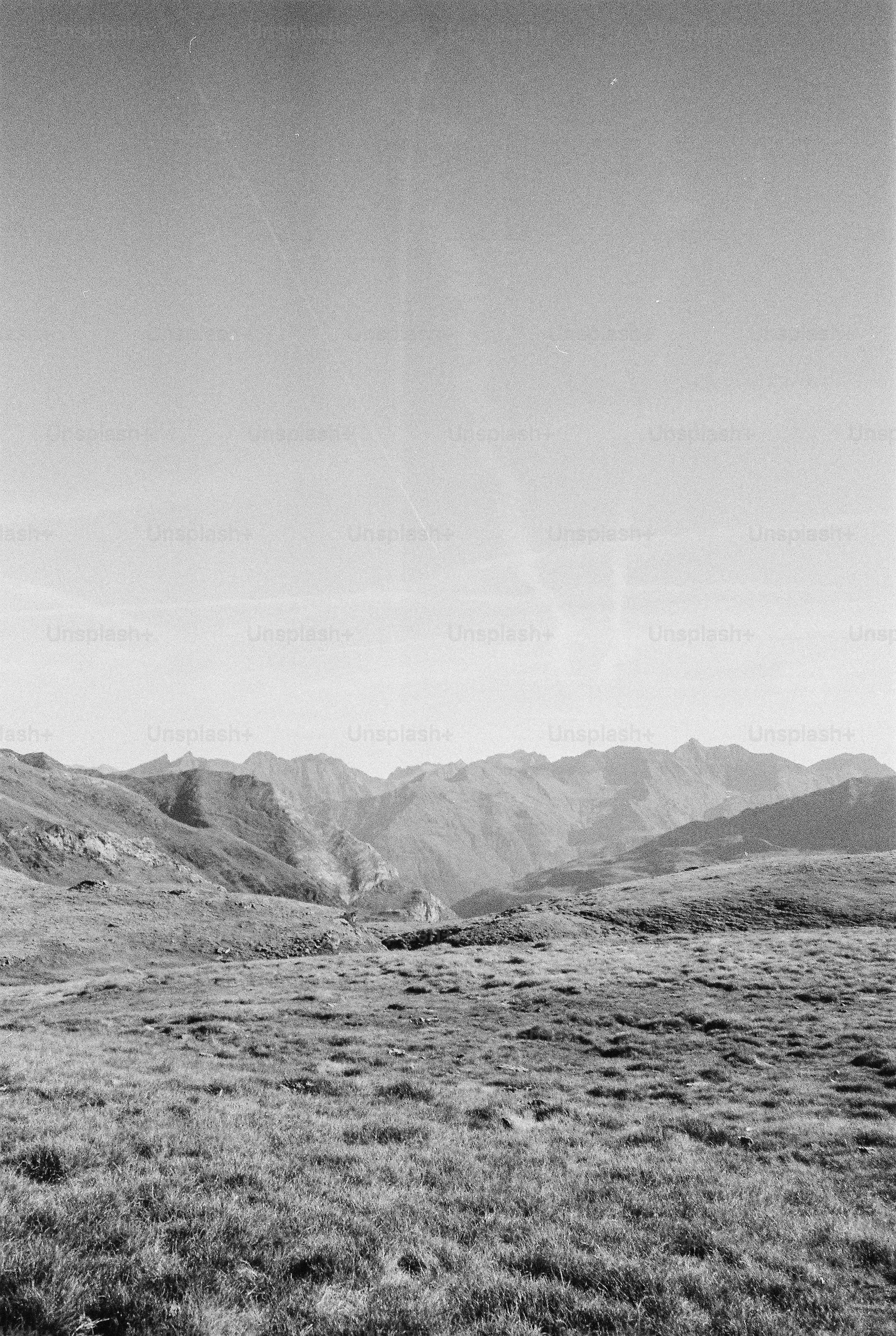 A black and white landscape of grassy hills leading to distant mountain peaks