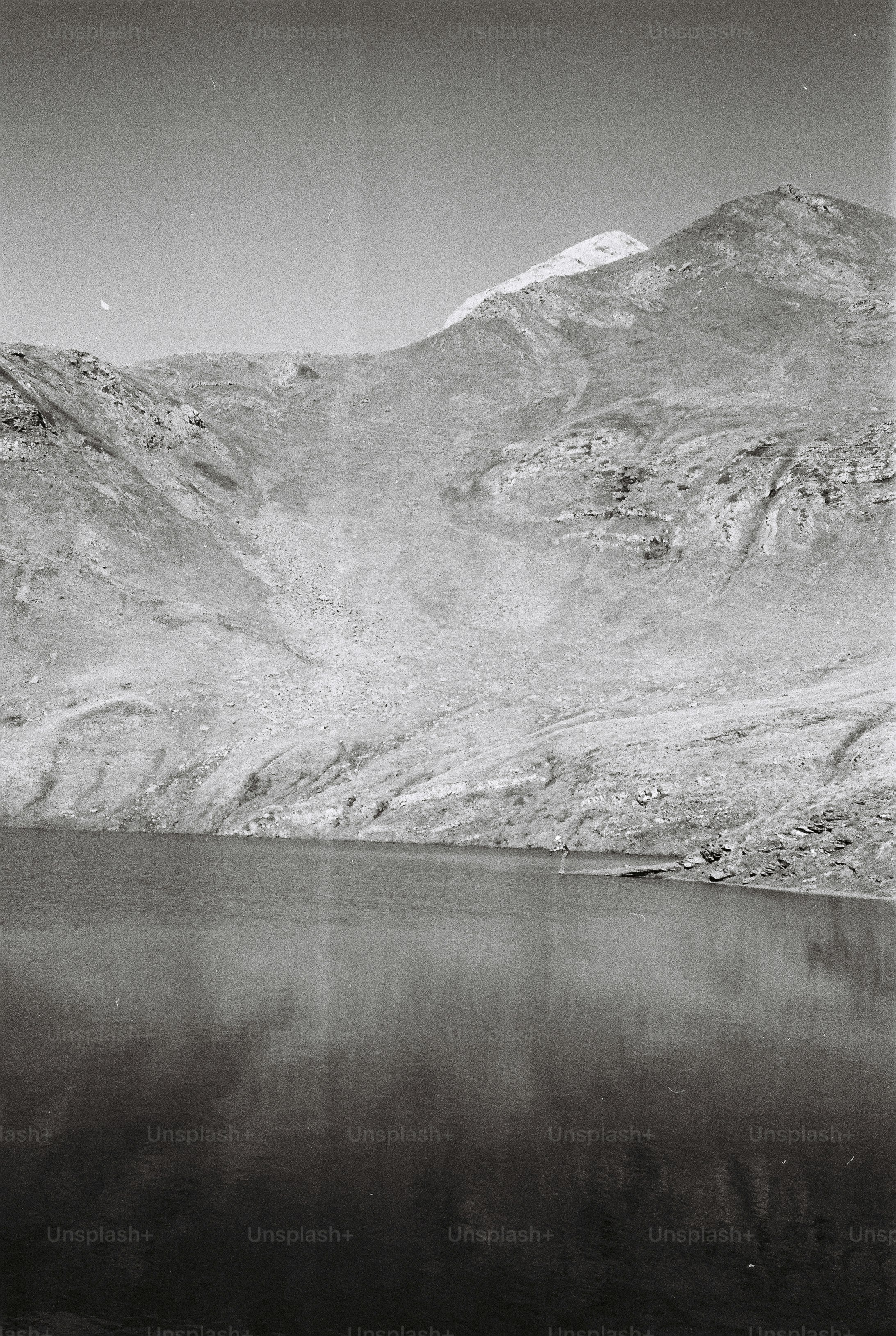 A person standing on the shore of a mountain lake beneath rocky slopes