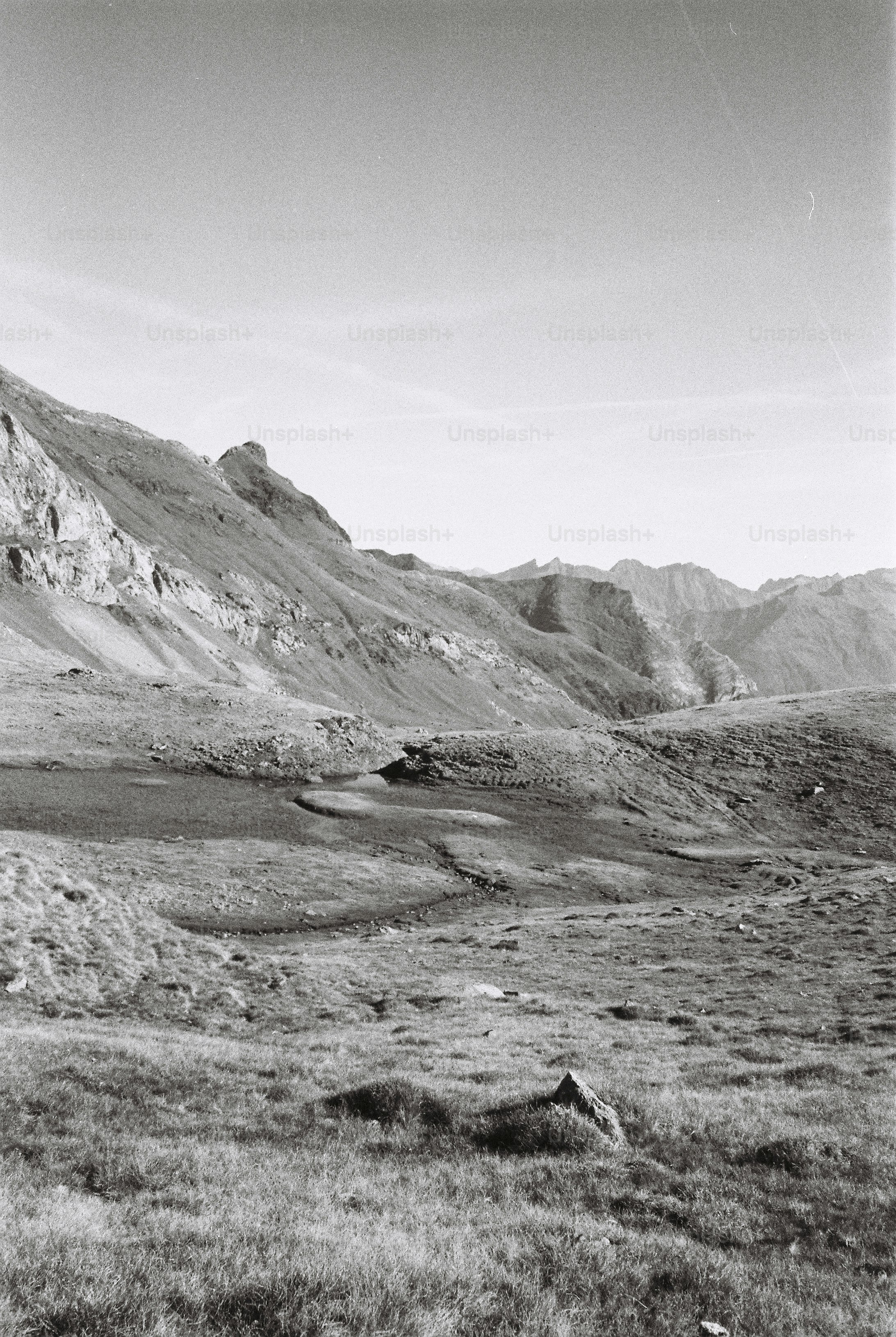 A black and white landscape of grassy mountain slopes and a small pond