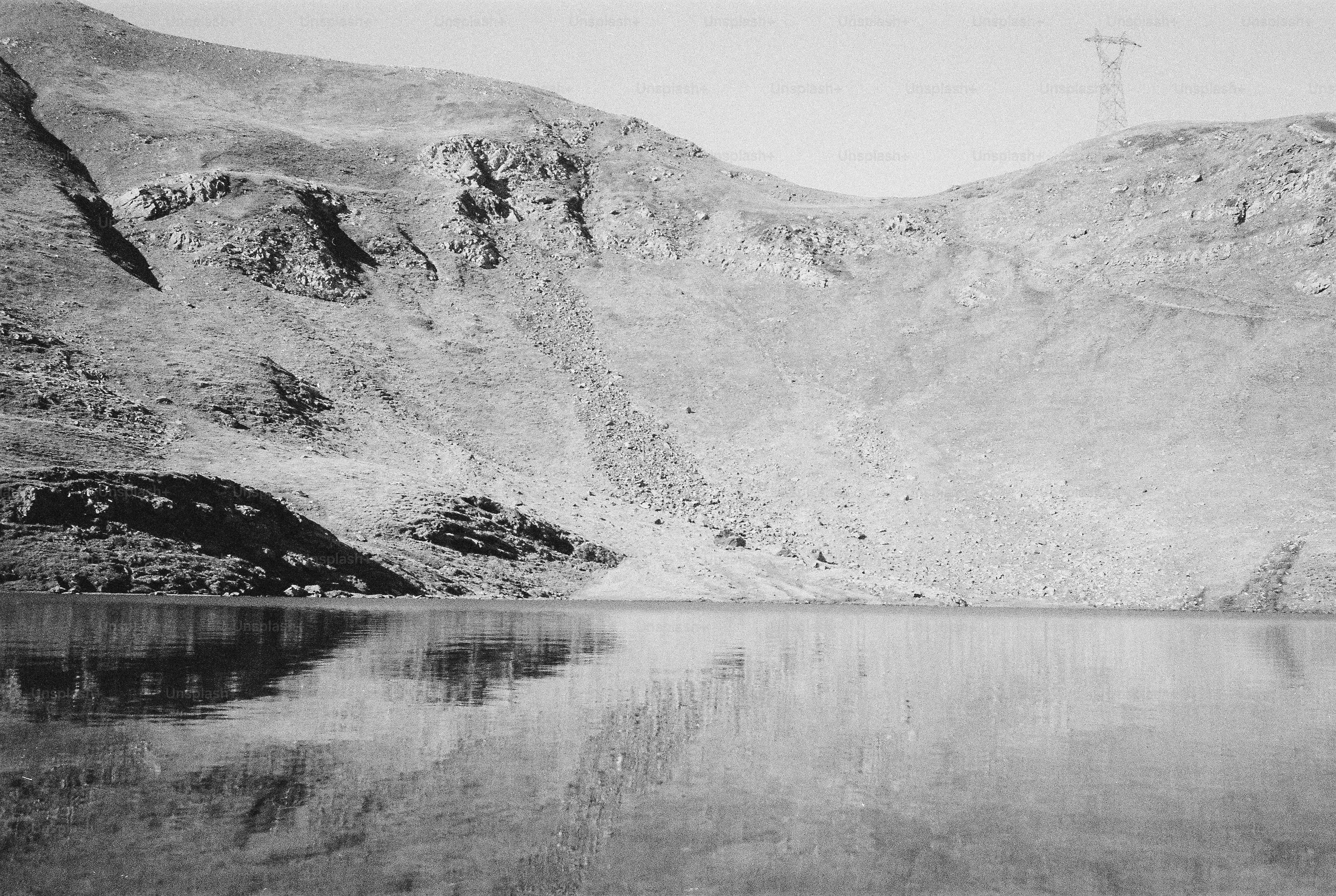A calm mountain lake reflecting a barren rocky slope under a clear sky