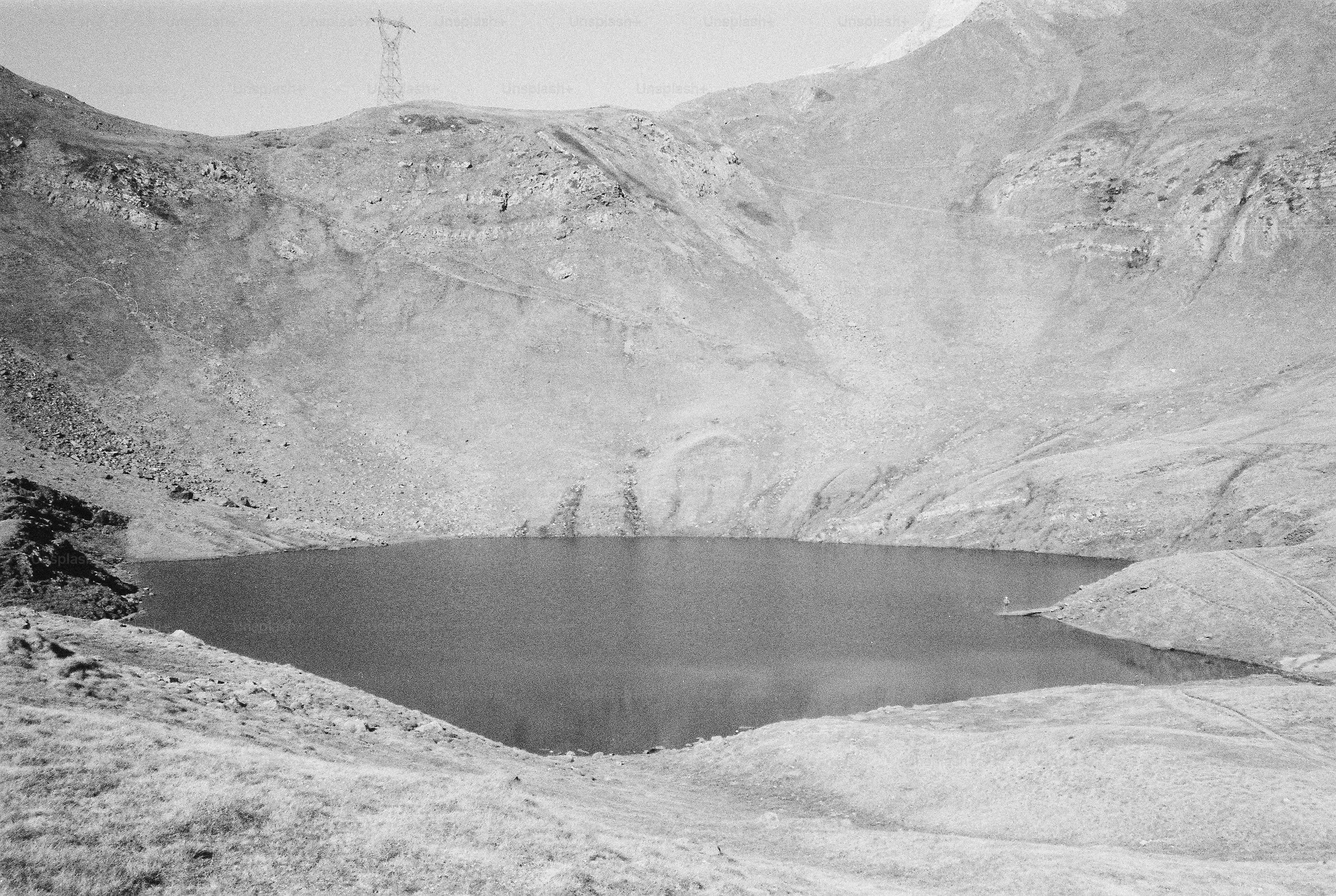A dark mountain lake in a rocky basin with a transmission tower above