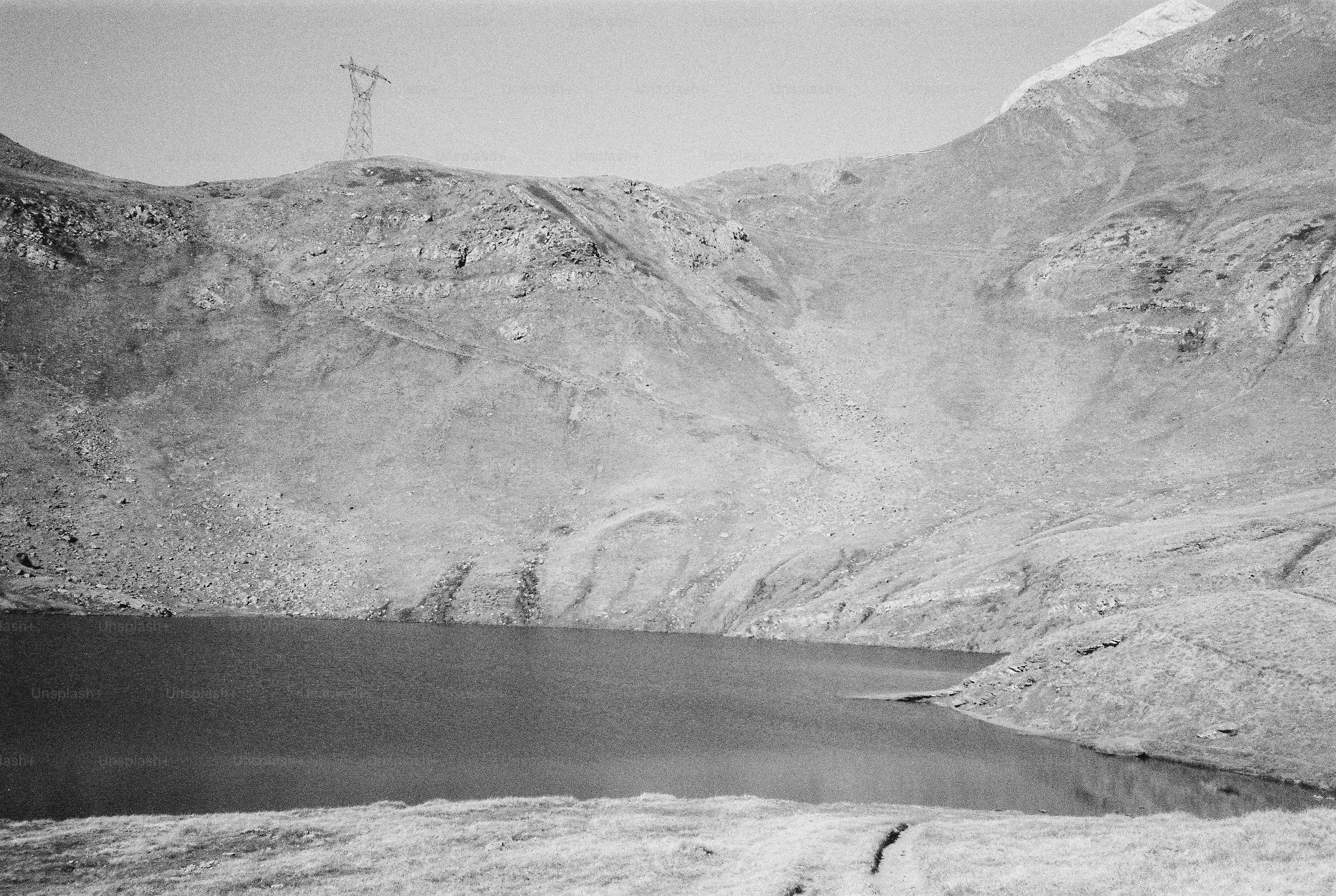 A mountain lake below a rocky slope with a transmission tower on the ridge