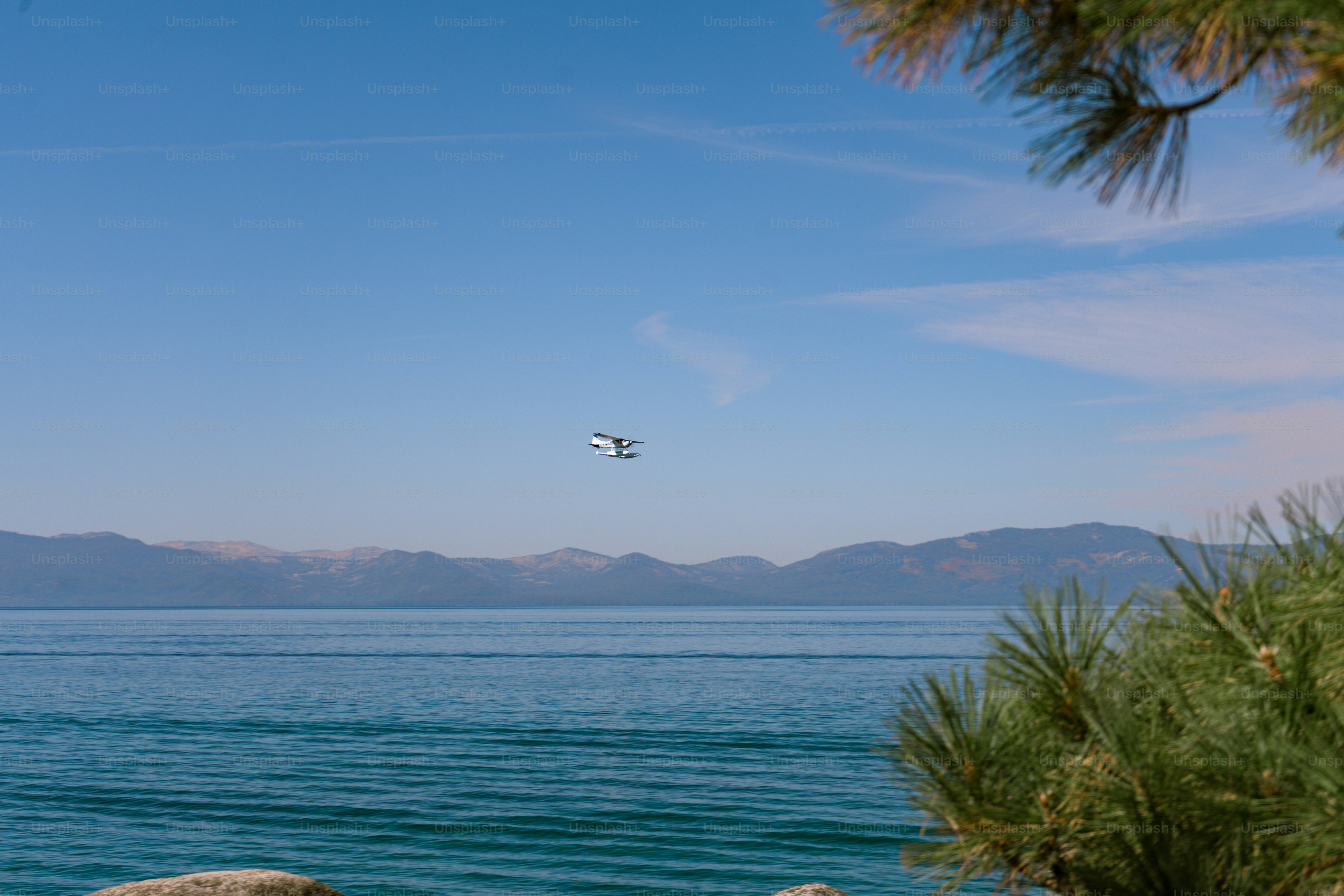 A small seaplane flying over a large blue lake with distant mountains