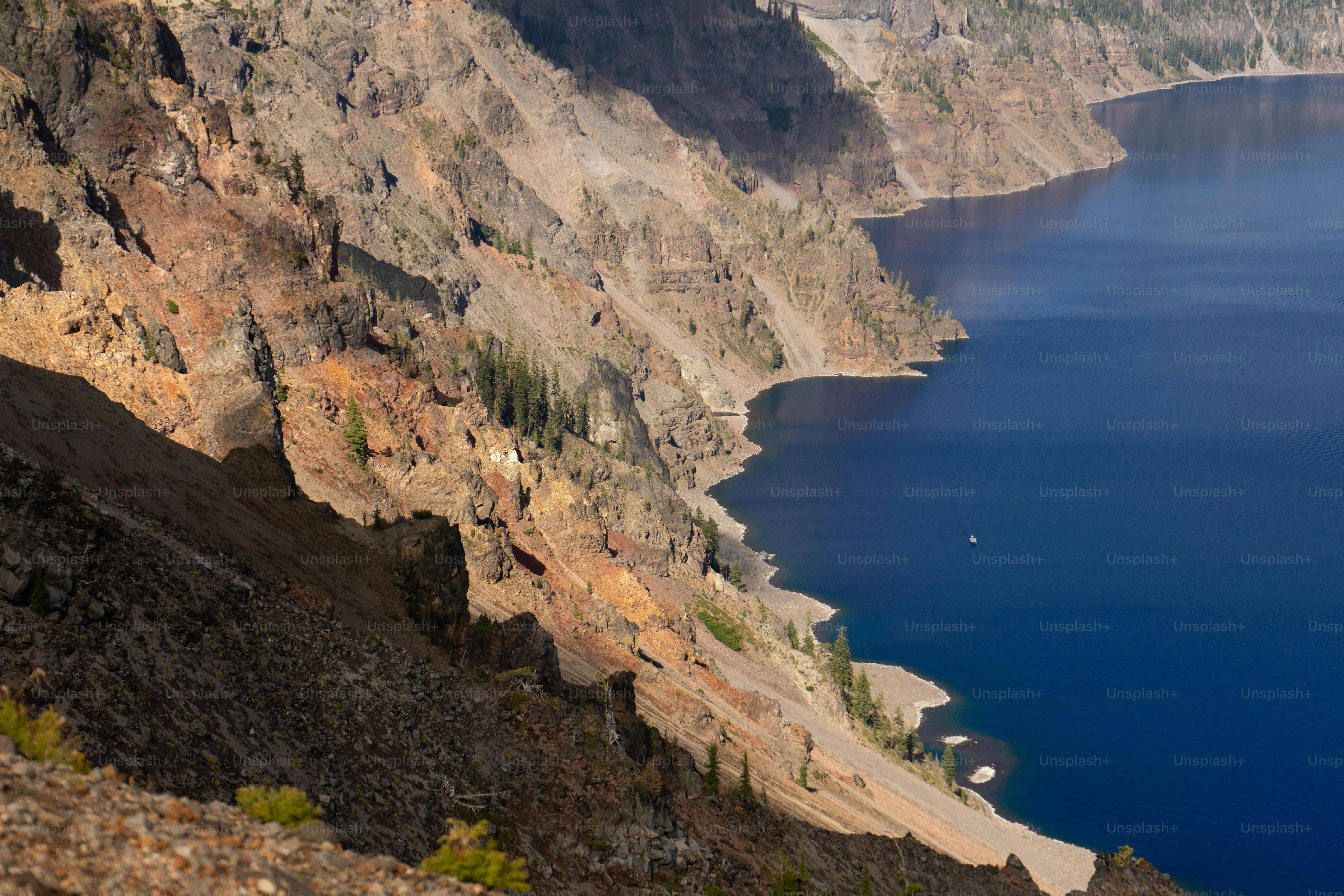 A steep rocky cliffside overlooking a deep blue lake with a small boat