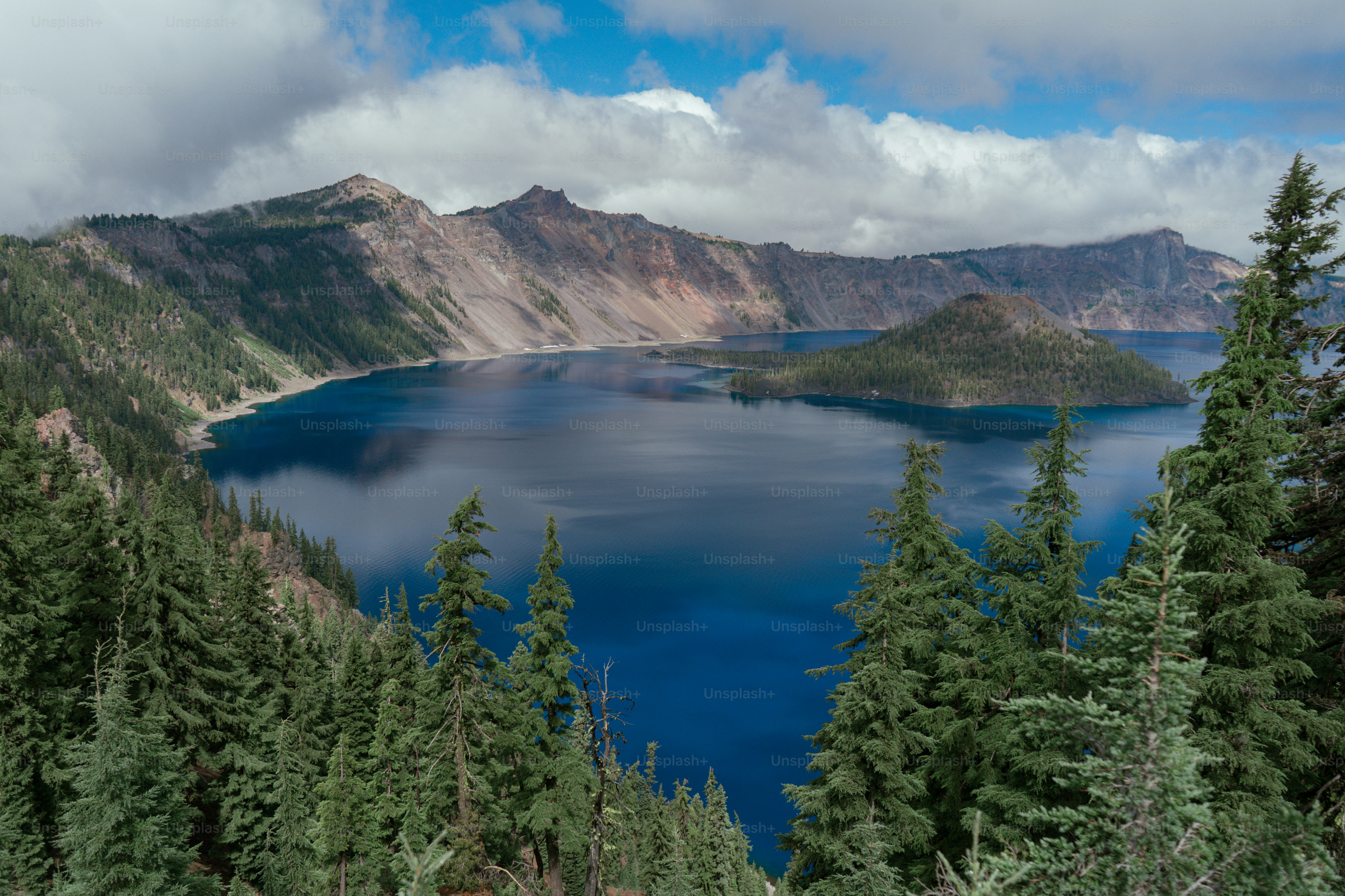 A deep blue lake surrounded by steep mountains and evergreen trees under cloudy skies
