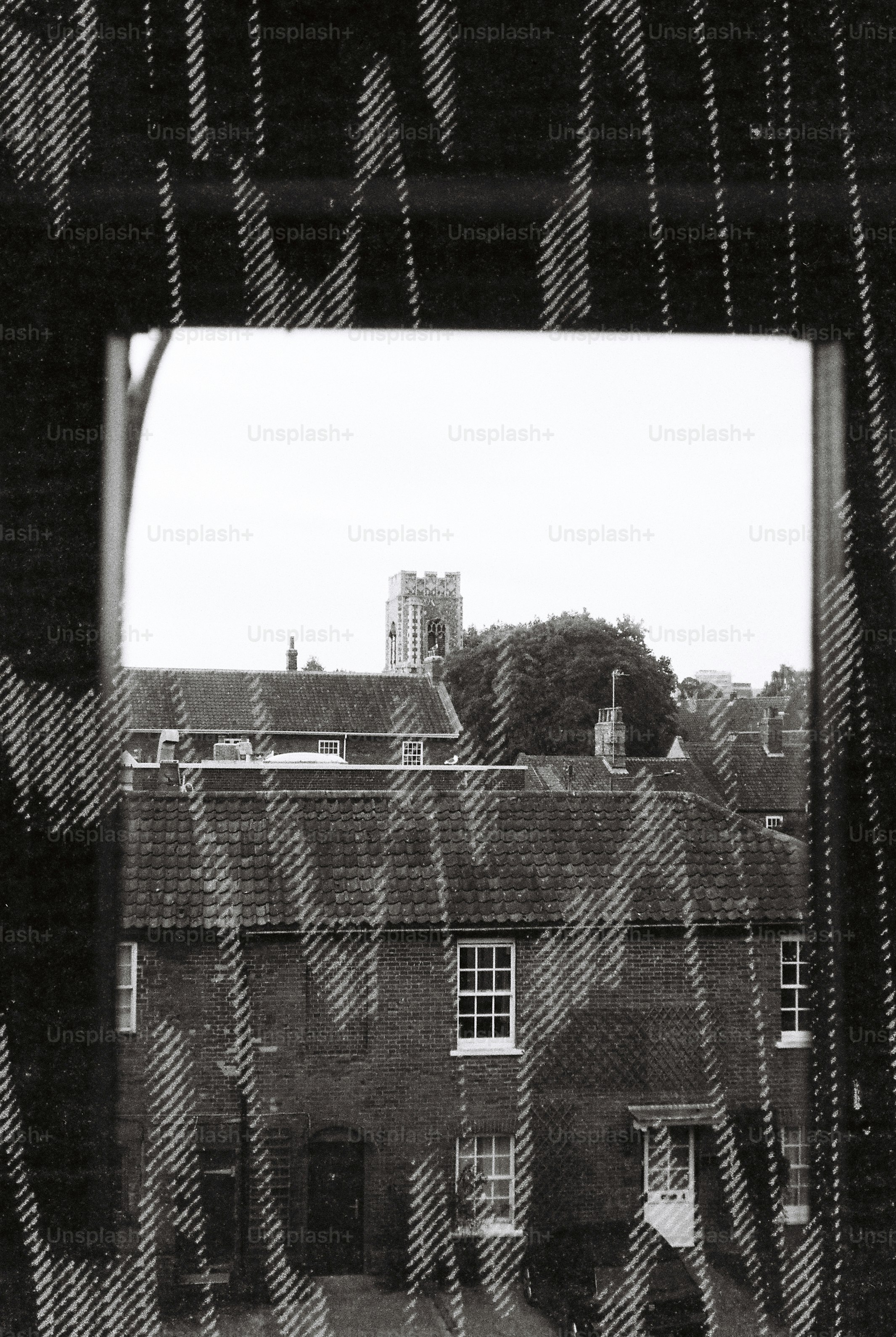 A view of brick houses and a church tower through a patterned curtain